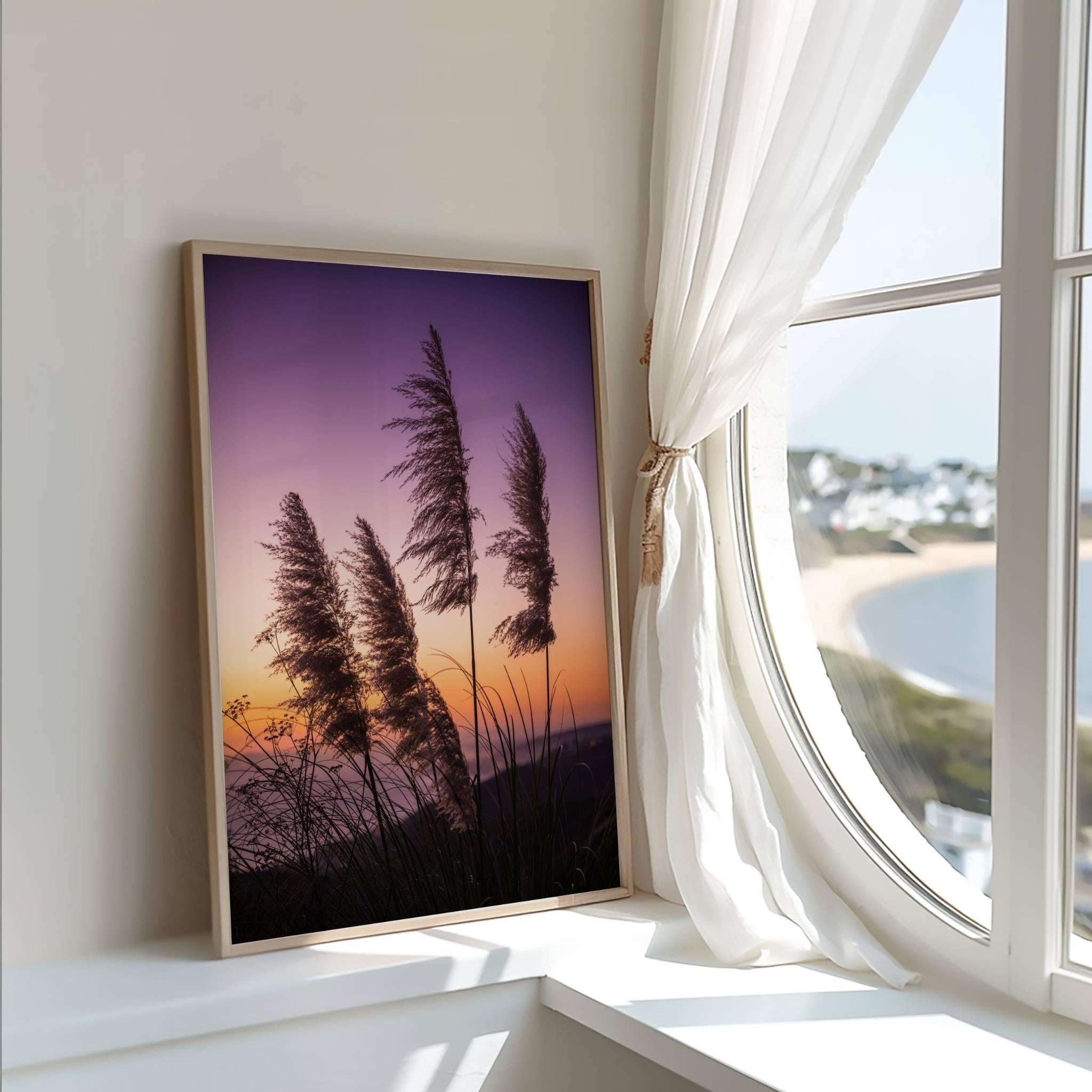 Framed coastal pampas grass sunset wall art by Abigail Diane Photography displayed beside a sunlit window in a bright coastal-inspired room.