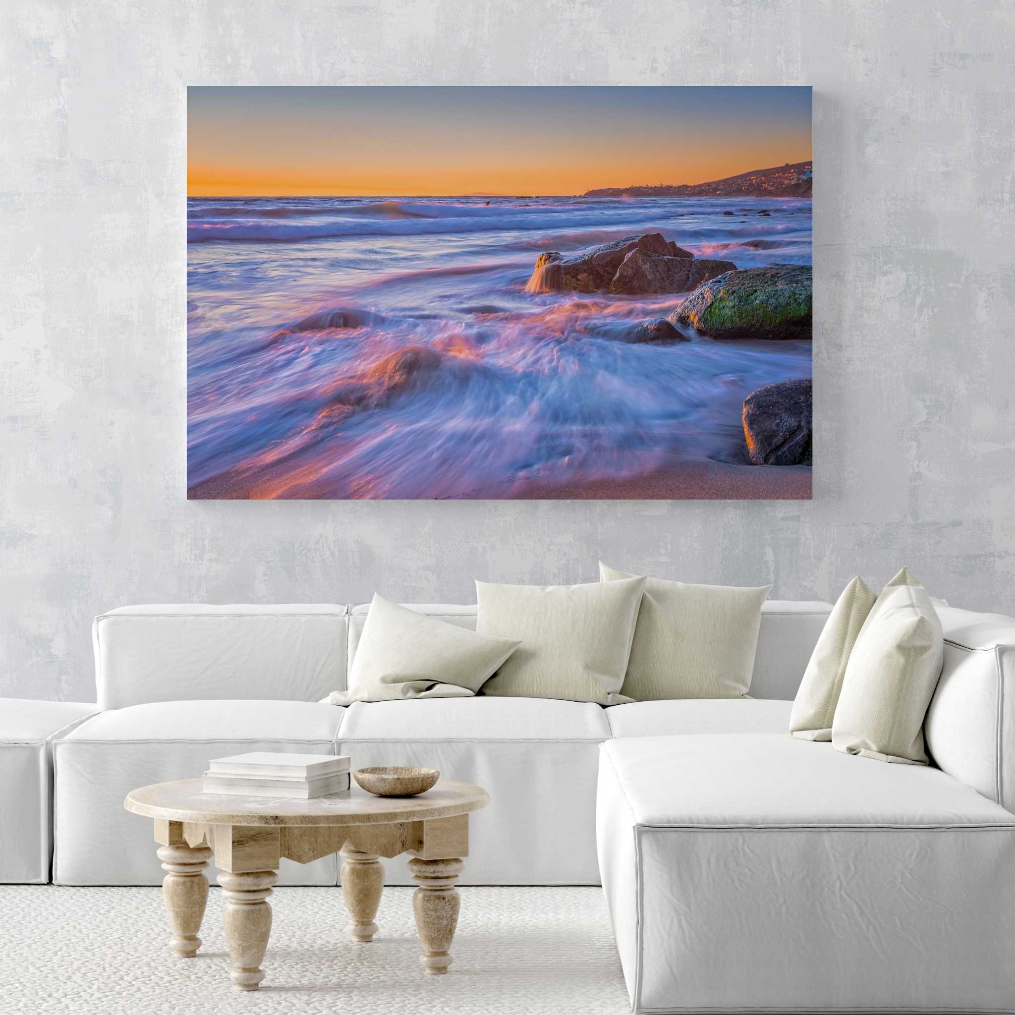 Large Cotton Candy Waves dye-sublimation metal print by Abigail Diane Photography displayed above a white sectional sofa, featuring pastel waves flowing over the shoreline at sunset in Laguna Beach, California.