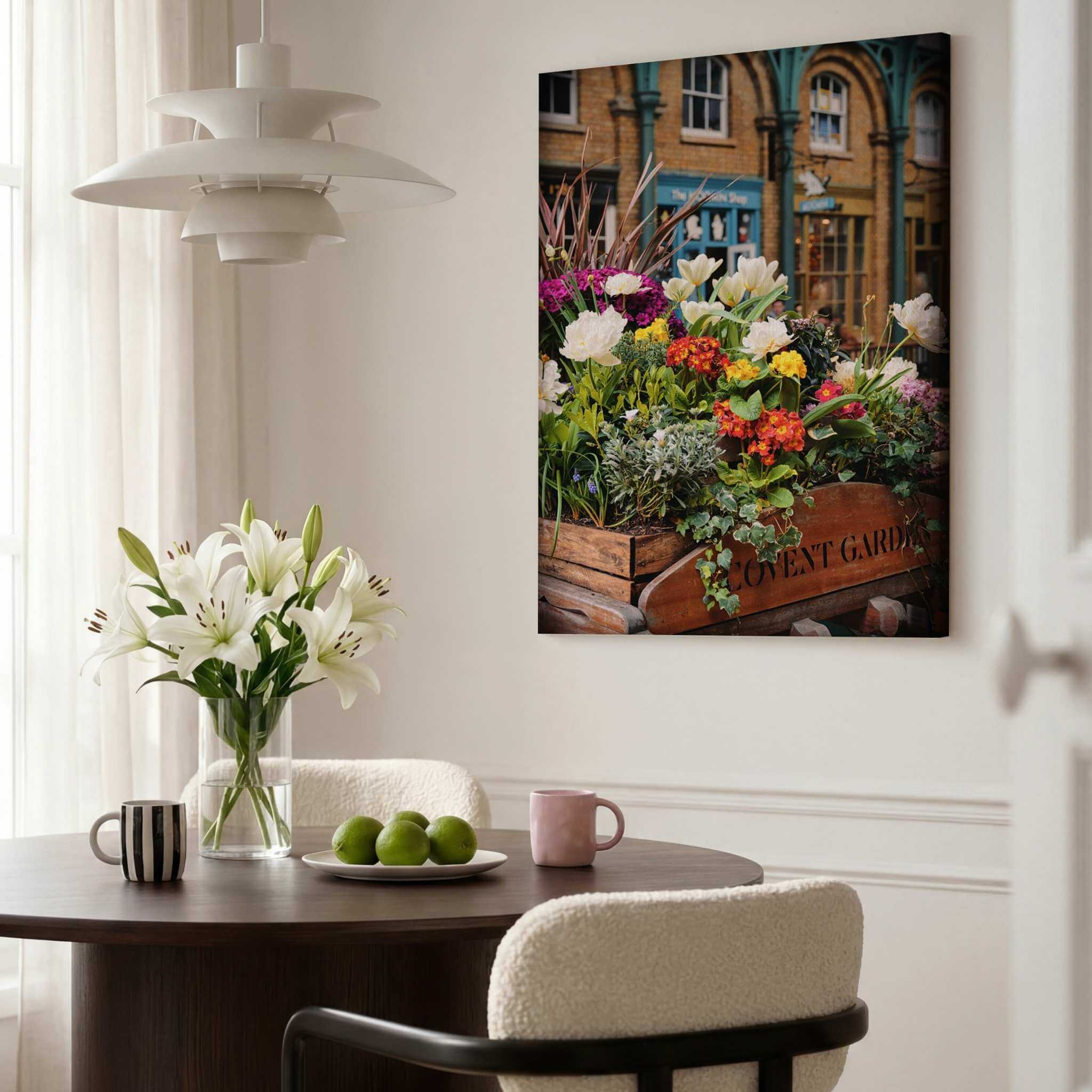 Close-up of Covent Garden in Bloom by Abigail Diane Photography displayed as a large vertical canvas print in a contemporary dining room with white lilies, green apples and a dark wood table, featuring vibrant floral displays in Covent Garden, London.
