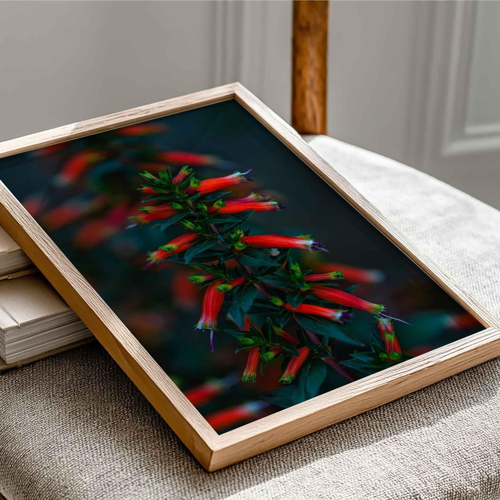 Close-up of Crimson Whispers at Twilight framed fine art print by Abigail Diane Photography resting on stacked books, featuring a vibrant red firecracker plant botanical photograph in a natural oak frame.