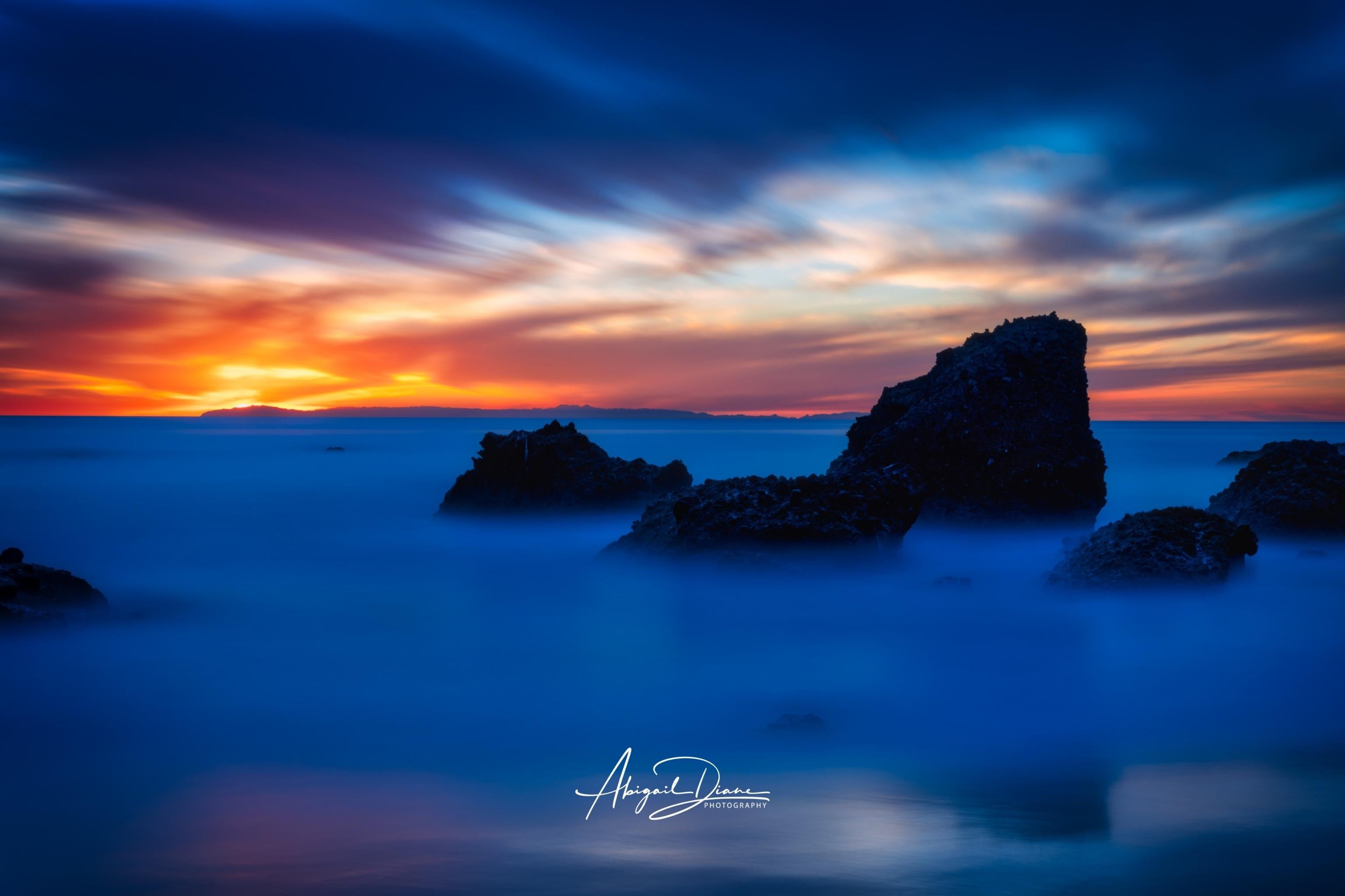 Escape to a Mystical Blue Hour fine art photograph by Abigail Diane Photography featuring a tranquil blue-hour sunset over the Pacific Ocean with dramatic sea stacks, silky long-exposure water, and glowing orange skies at Laguna Beach, California.