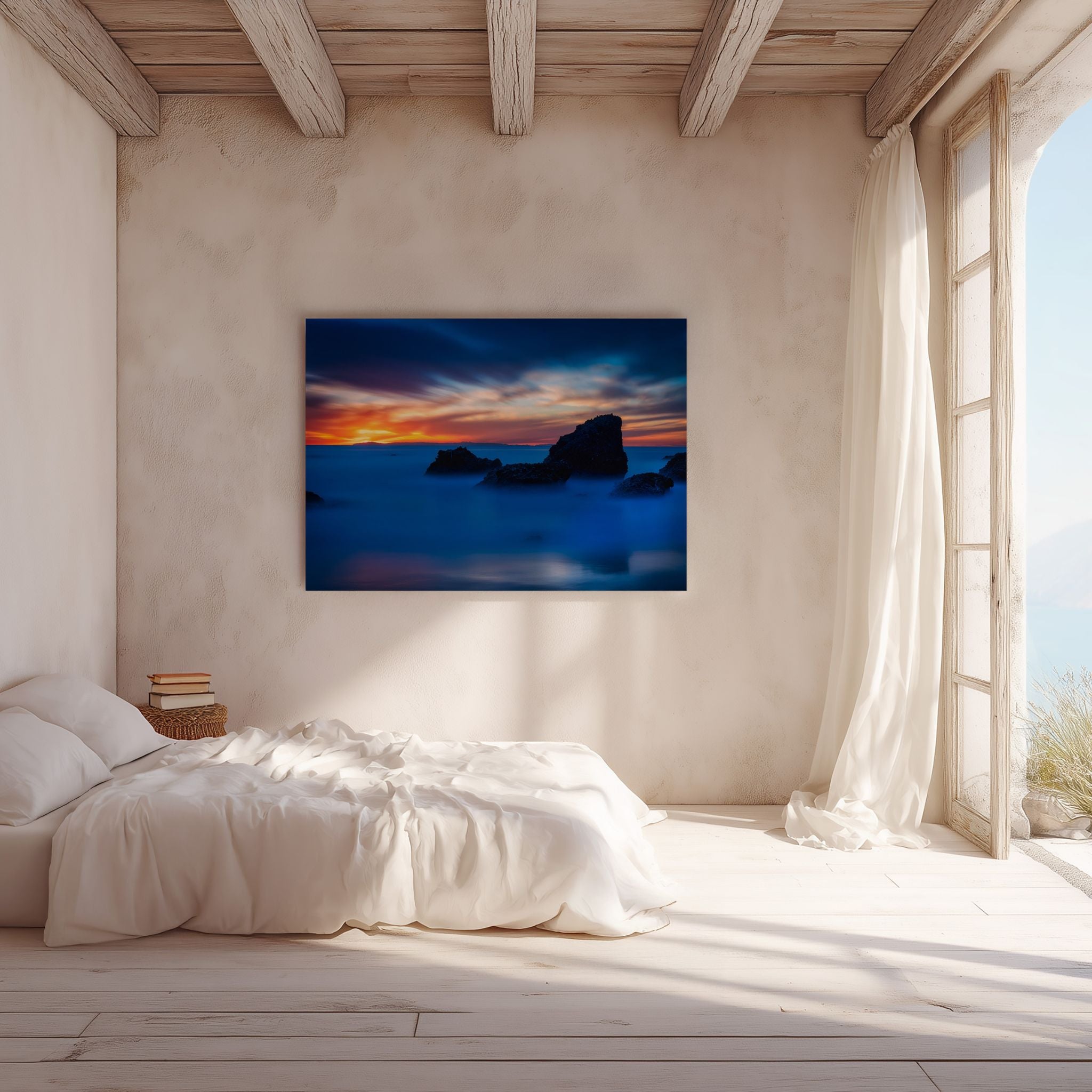 Escape to a Mystical Blue Hour metal print displayed above a white bed in a serene coastal bedroom, featuring a long-exposure California seascape with silhouetted rocks, silky blue water, and glowing sunset light across the horizon.