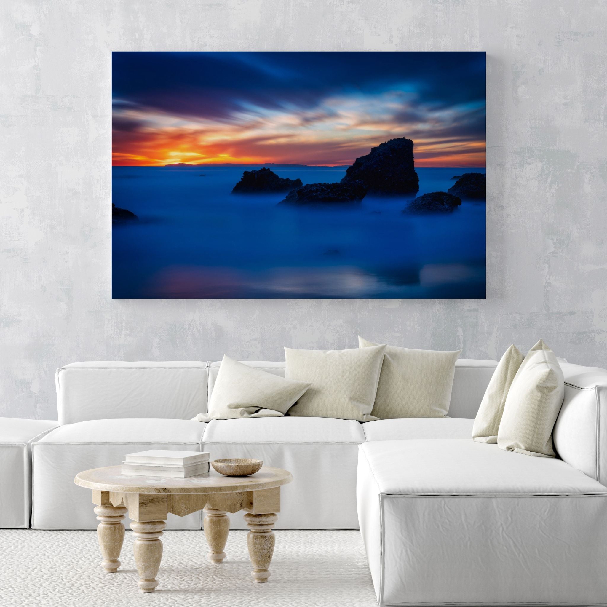 Escape to a Mystical Blue Hour high-definition metal print displayed above a white sectional sofa in a contemporary living room, highlighting the dramatic contrast of deep blue ocean tones and fiery sunset colors from Laguna Beach, California.