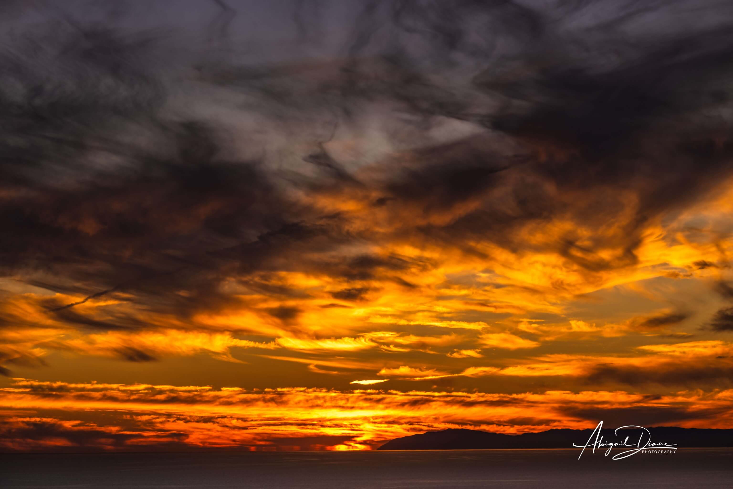 Dramatic golden sunset over the Pacific Ocean with glowing clouds and deep orange tones, fine art seascape photography by Abigail Diane Photography.