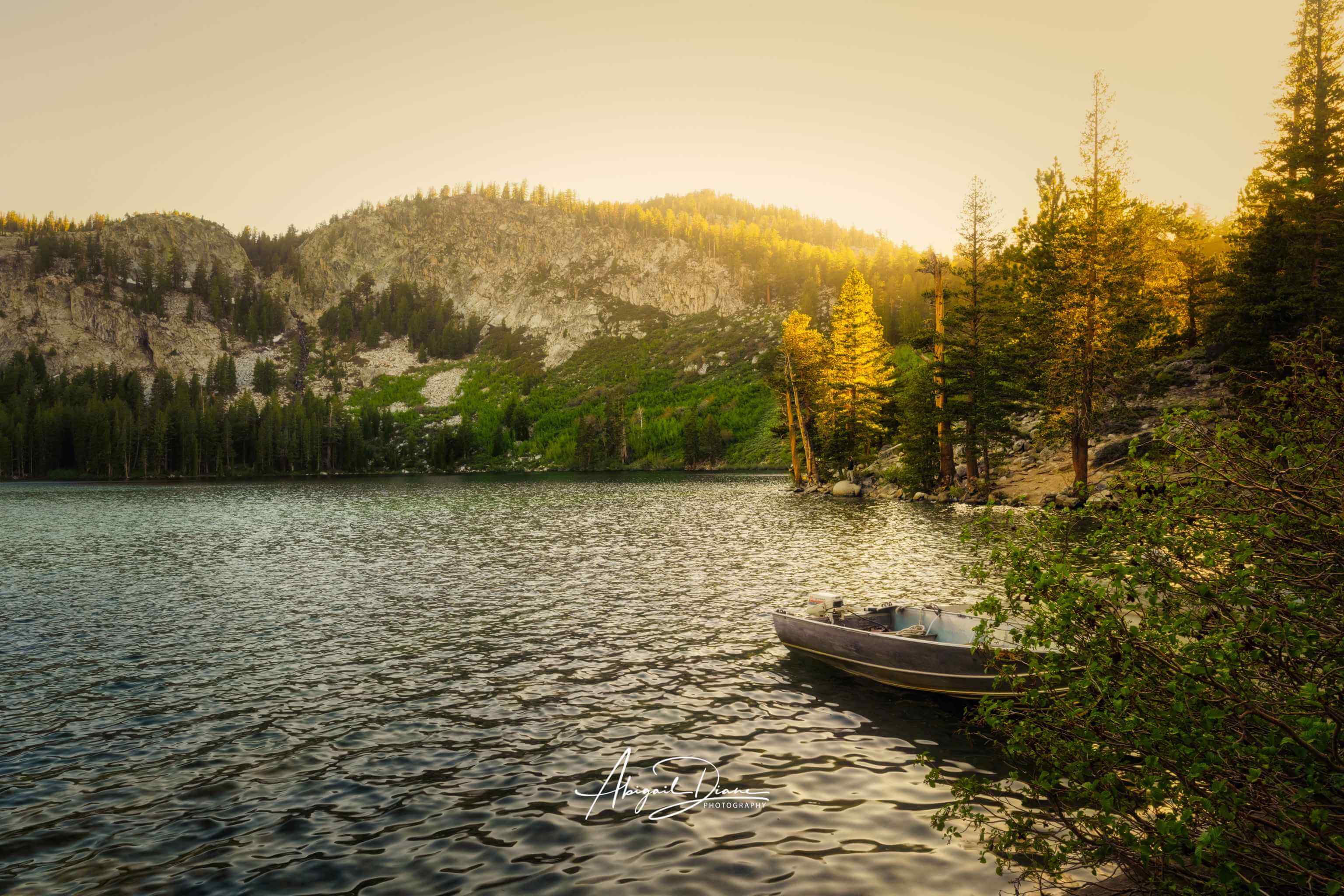 Golden Hour on the Alpine Lake, a peaceful alpine lake near Mammoth Lakes in California’s Eastern Sierra, with a small boat beneath sunlit pines and rugged mountains.