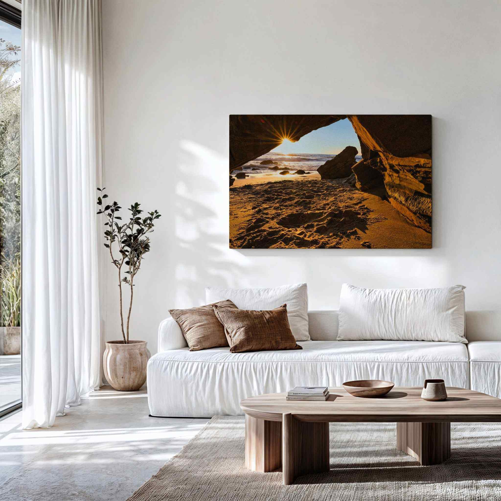 Gallery wrapped canvas of Golden Hour Sunburst displayed above a modern white sofa, featuring a sunburst through sea caves at Laguna Beach, California. Fine art wall decor by Abigail Diane Photography.