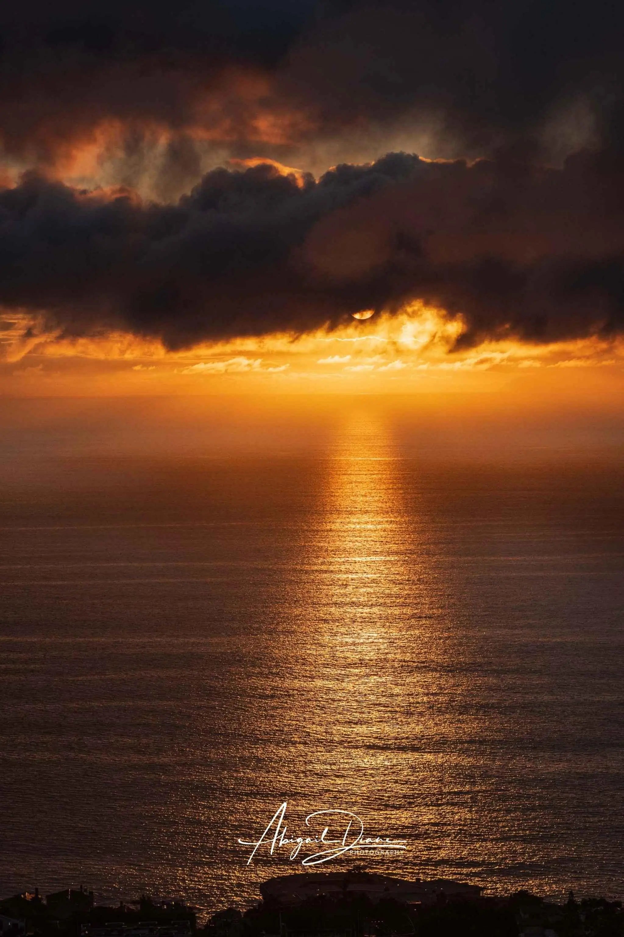 Golden Rays on the Mirrored Sea of the Pacific by Abigail Diane Photography showing a dramatic golden sunset over calm ocean waters with sun rays reflecting across the sea beneath dark clouds at golden hour.