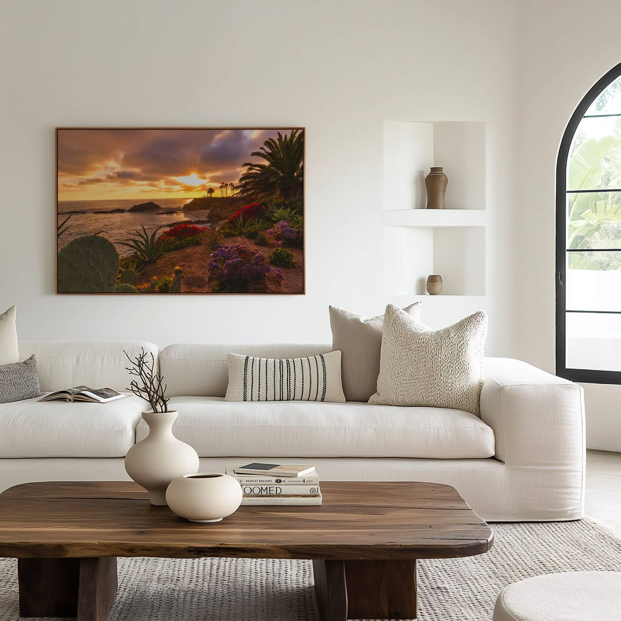 Laguna Beach sunset wall art displayed above a modern white sofa, featuring dramatic golden light over the Pacific Ocean framed by colorful coastal gardens and palm trees.