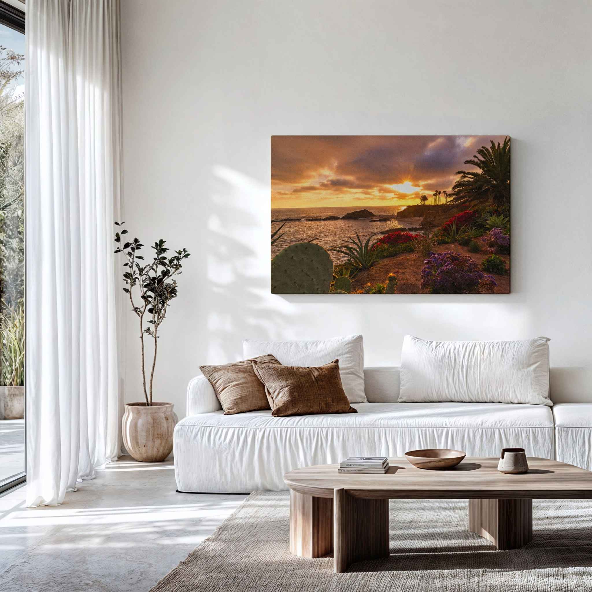 Gallery wrapped canvas featuring a Laguna Beach sunset with palm trees, coastal cliffs, and blooming flowers displayed above a white sofa in a minimalist coastal living room.