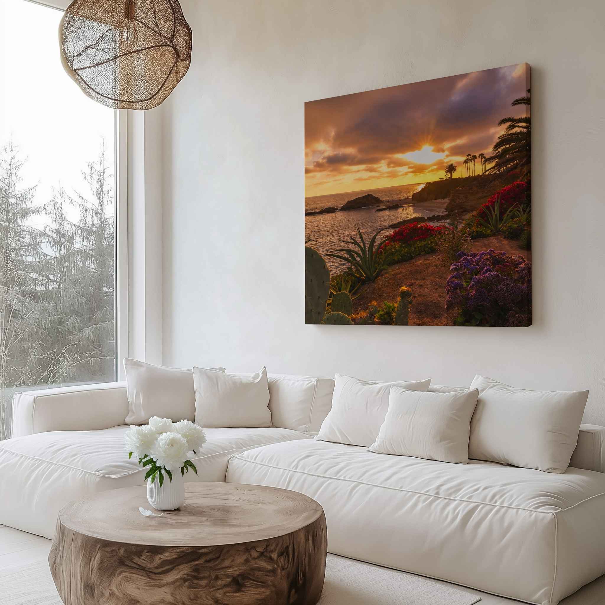 Gallery wrapped canvas featuring a Laguna Beach sunset with palm trees, coastal cliffs, and vibrant flowers displayed above a white sectional sofa in a modern living room.