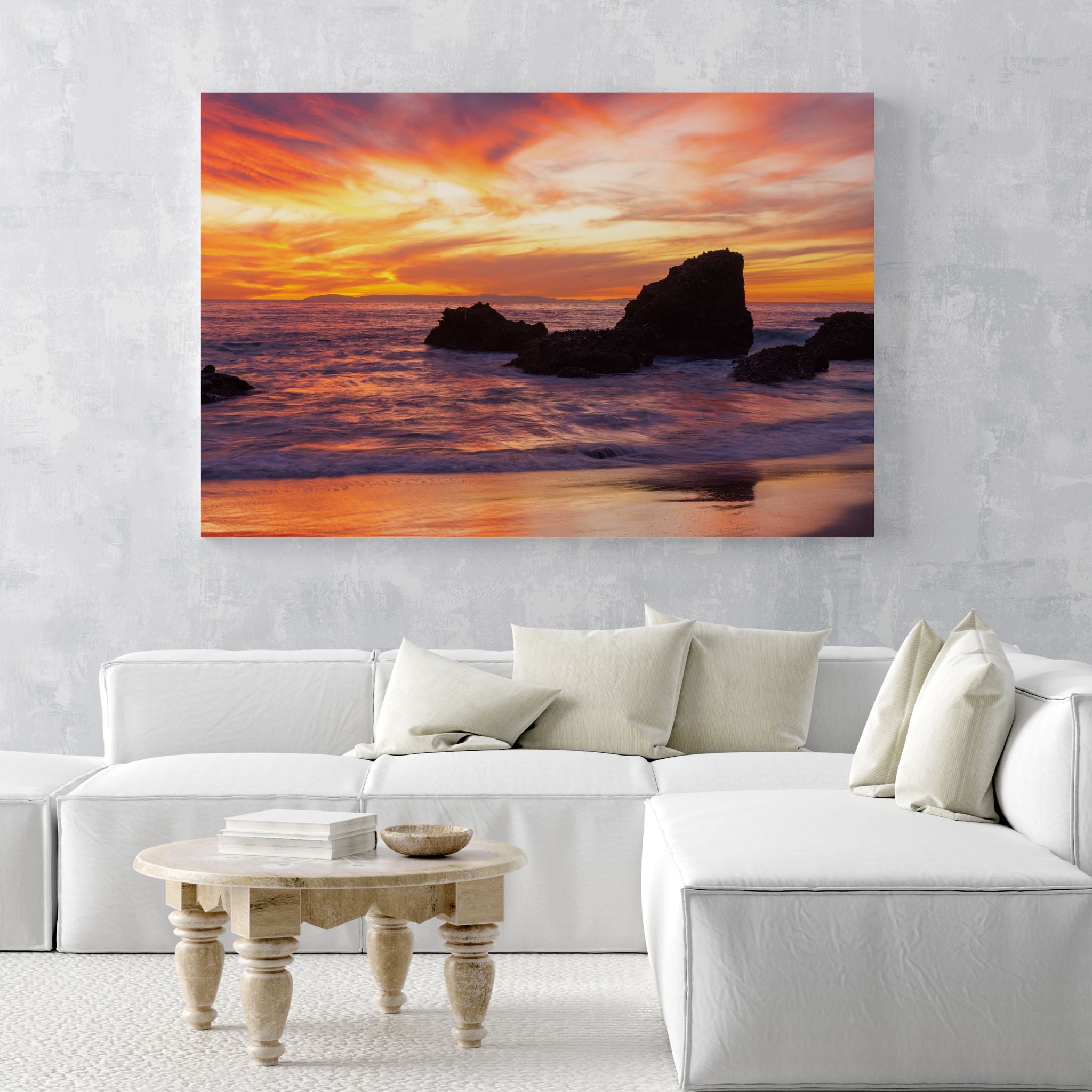 Large metal wall art of Woods Cove Beach, Laguna Beach, displayed above a contemporary white sectional sofa, showcasing a dramatic California sunset by Abigail Diane Photography.
