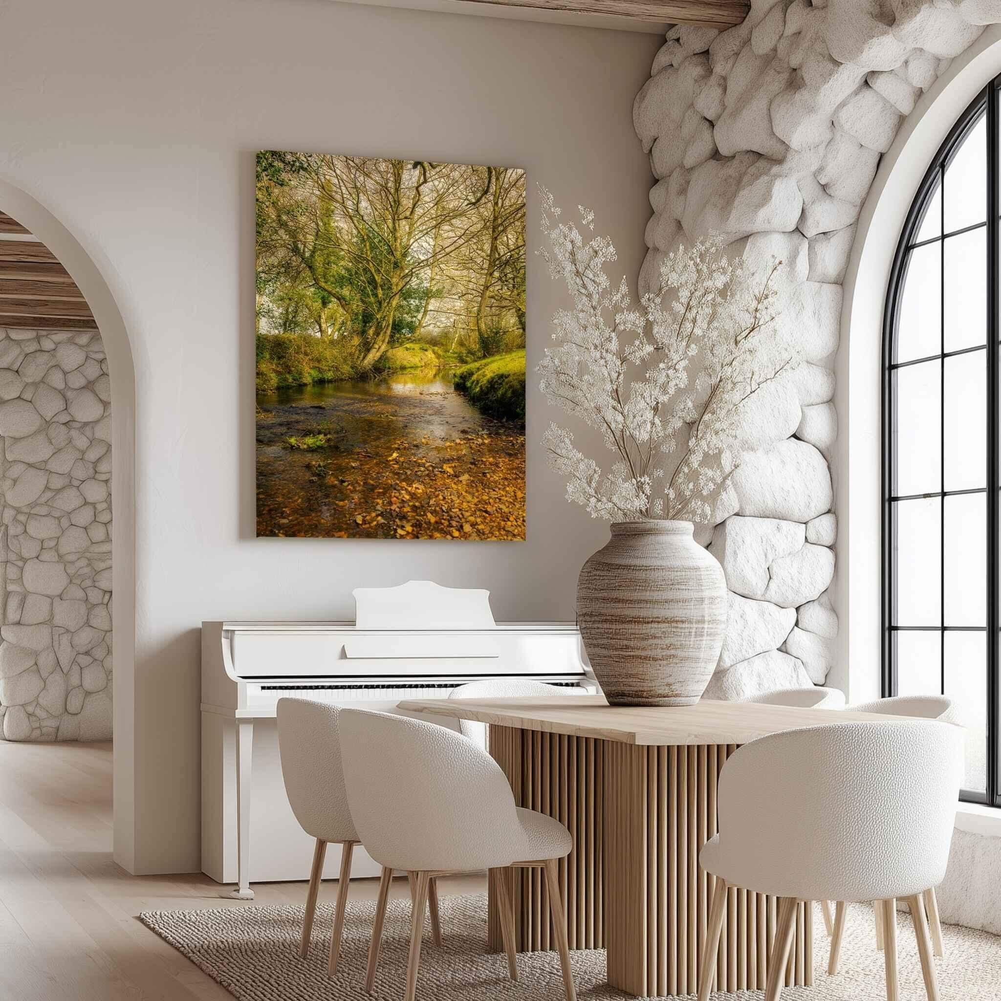 Large gallery-wrapped canvas print of Lazy Creek in the New Forest, UK by Abigail Diane Photography displayed above a white piano in a contemporary dining room with natural stone walls and soft daylight.