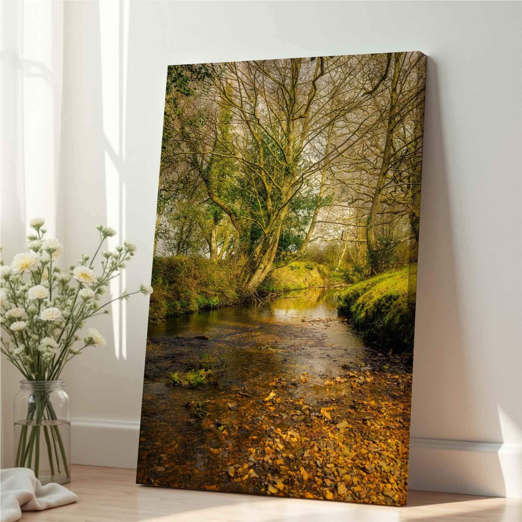 Gallery-wrapped canvas print of Lazy Creek in the New Forest, UK by Abigail Diane Photography leaning against a wall beside a glass vase of white flowers in soft natural light.