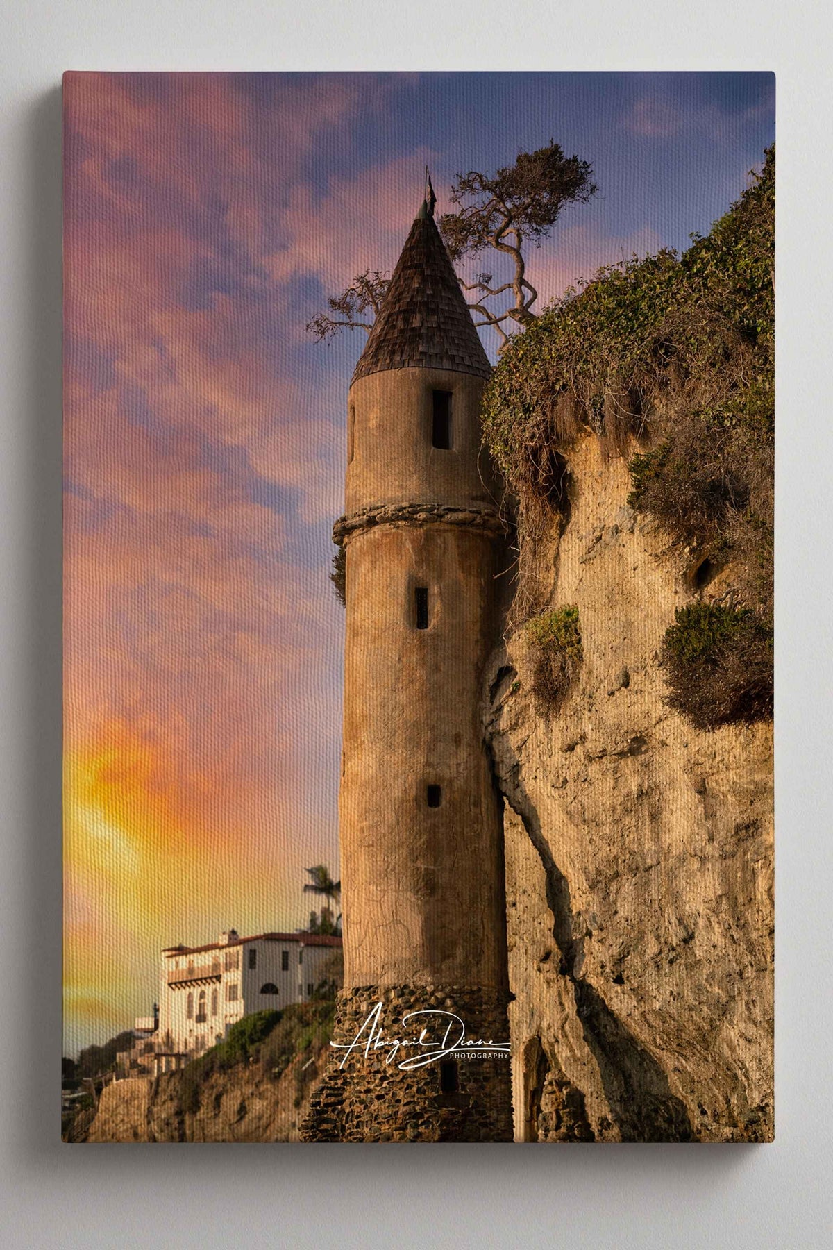 Let Your Hair Down canvas print featuring the iconic Pirate Tower at Victoria Beach in Laguna Beach, California, illuminated by warm golden light beneath soft pink and lavender sunset clouds, with Abigail Diane Photography branding.