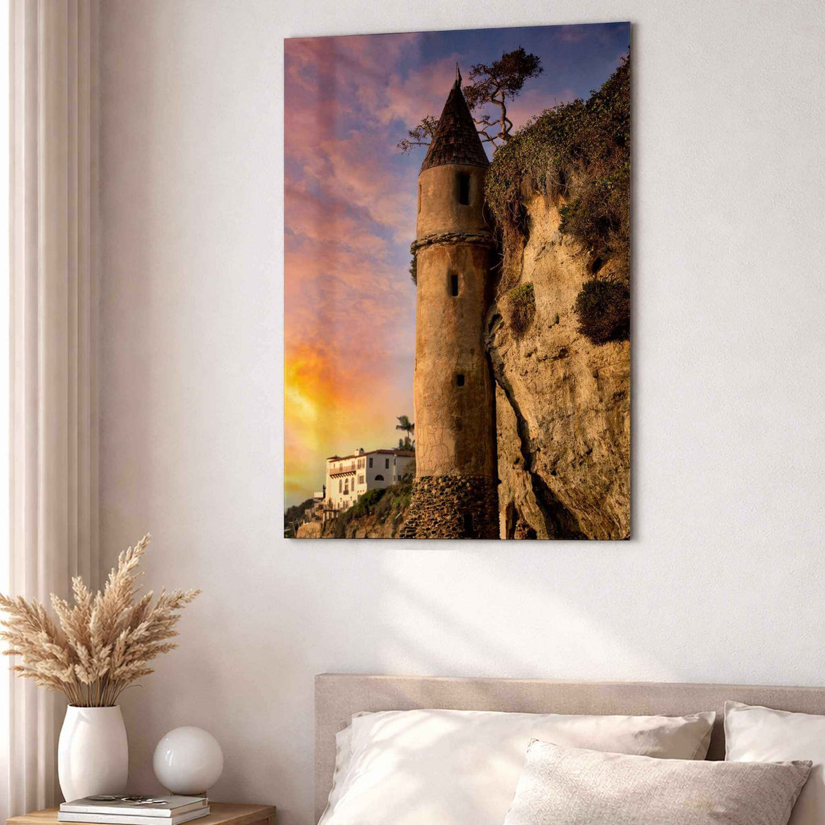Let Your Hair Down metal print displayed above a neutral bed in a warm minimalist bedroom, featuring the iconic Pirate Tower at Victoria Beach in Laguna Beach, California, glowing beneath a pink, orange, and blue sunset sky.