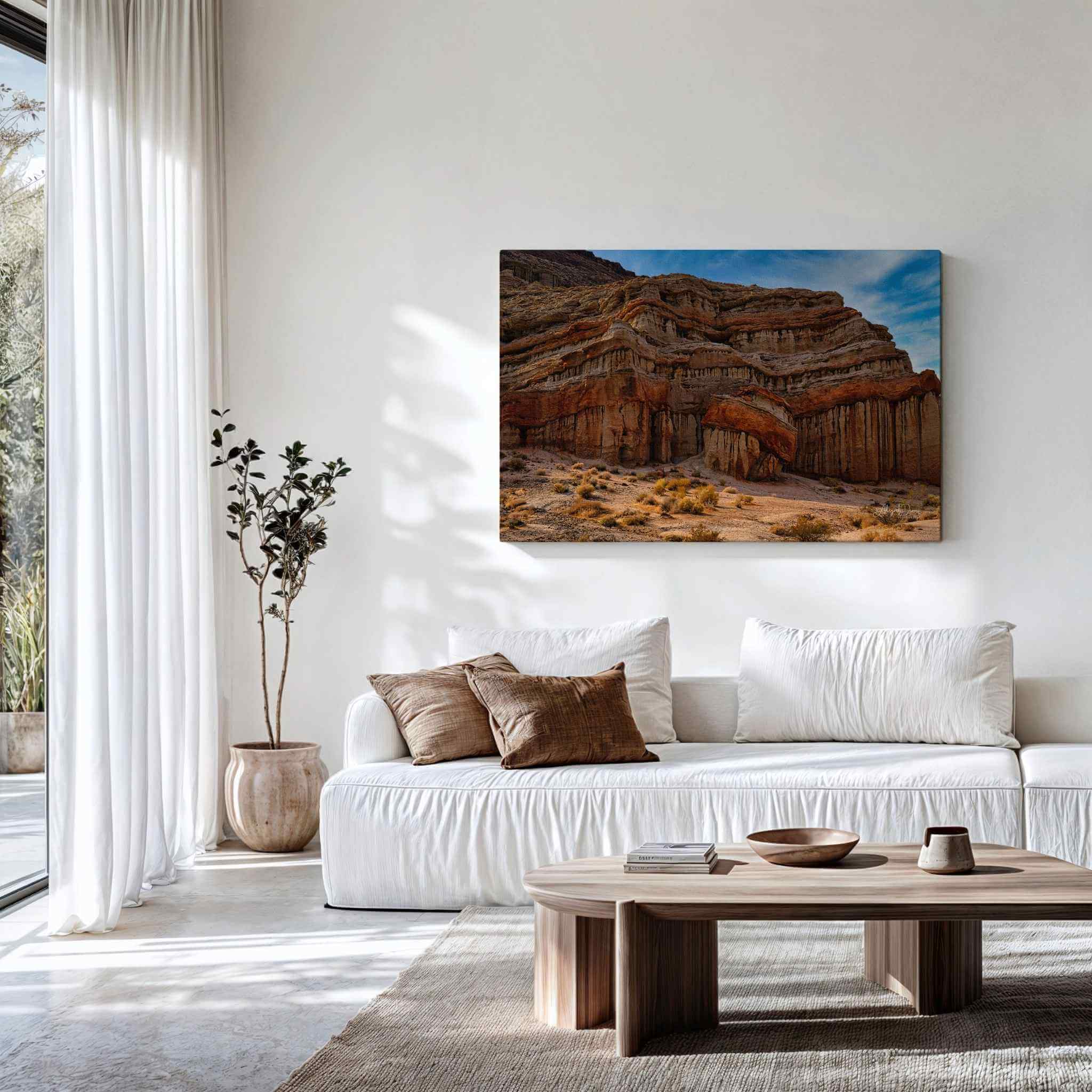 Large gallery-wrapped canvas of Red Rock Canyon State Park displayed above a cream sofa in a modern organic living room. The artwork features dramatic layered sandstone cliffs, sculpted desert rock formations, warm earth tones, and a vibrant blue sky, bringing the rugged beauty of California's Red Rock Canyon State Park into a contemporary home. Artwork by Abigail Diane Photography.
