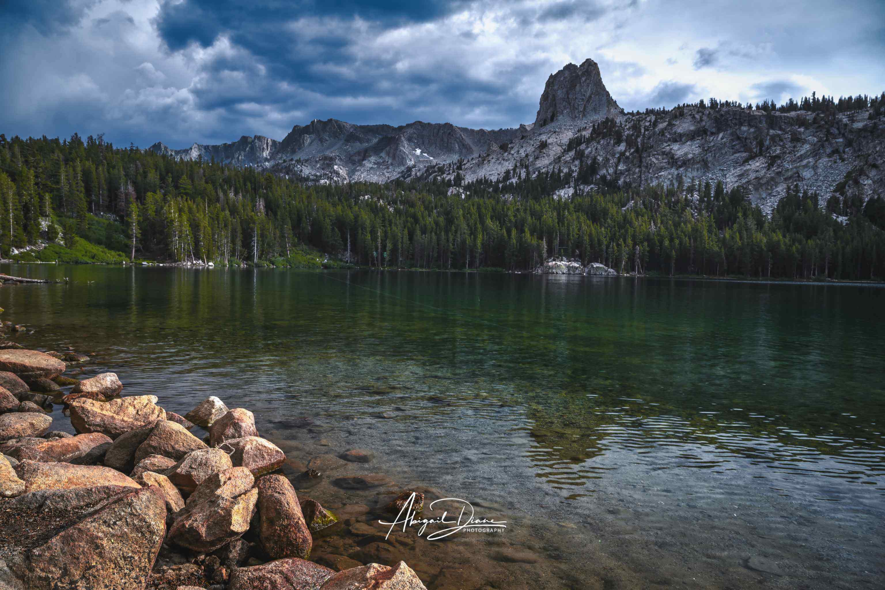 Reflections on Lake Mary in Mammoth Lakes, California, with crystal-clear alpine water, rugged mountain peaks, pine forest, and dramatic clouds in the Eastern Sierra , by Abigail Diane Photography