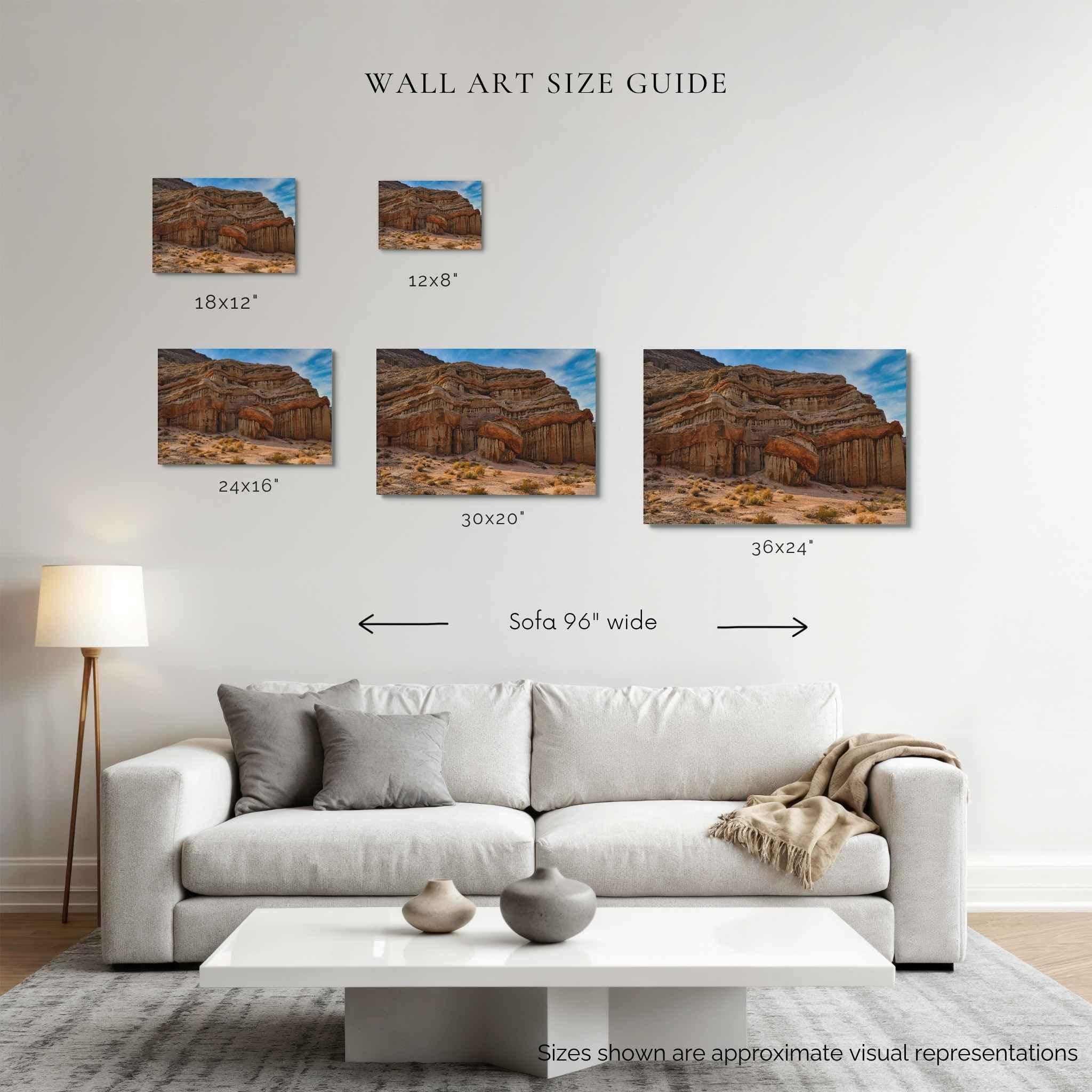 A wall art size guide displayed above a white sofa in a living room, showing five desert landscape canvas prints with dimensions labeled 18x12", 12x8", 24x16", 30x20", and 36x24", plus a sofa width reference.