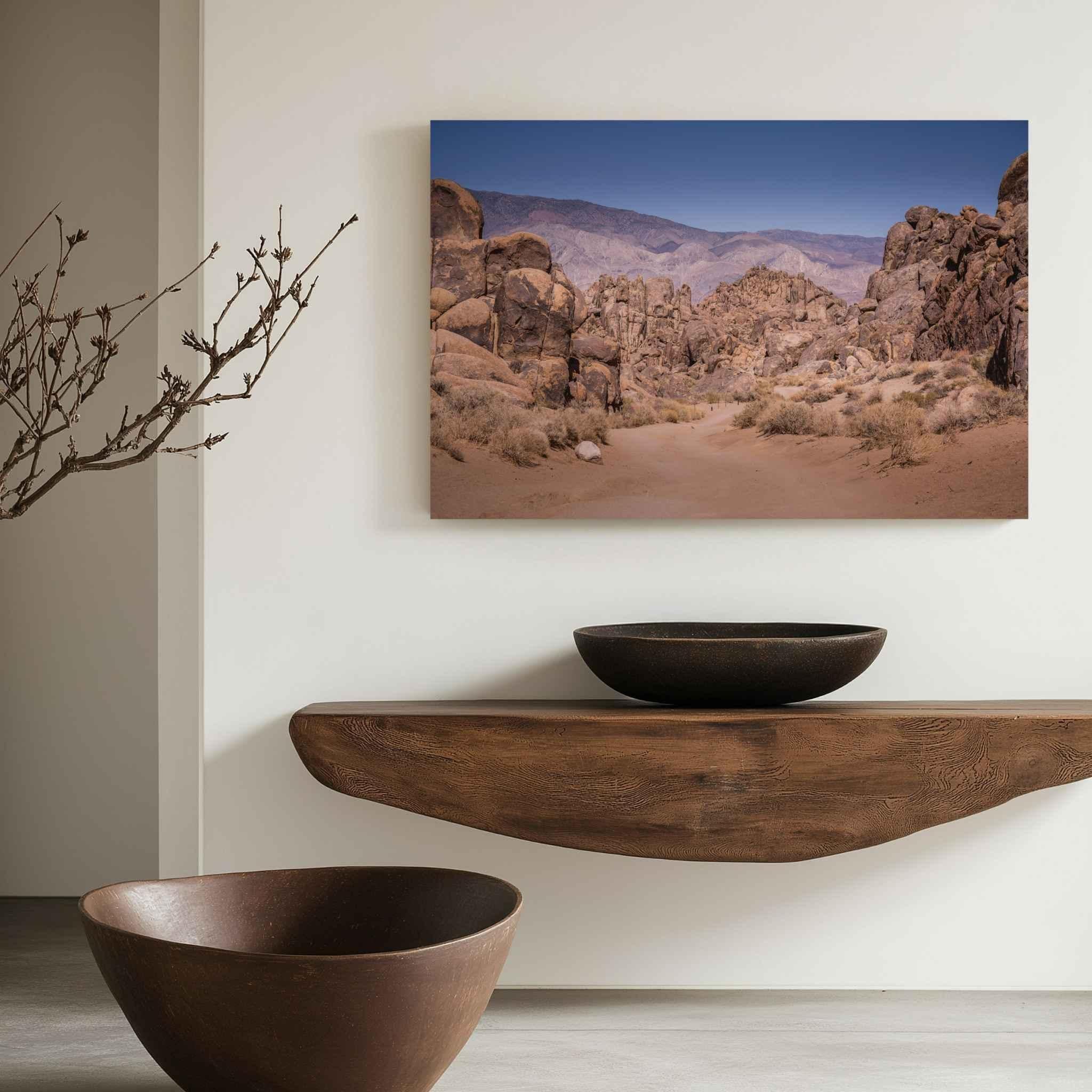 Sierra Desert Passage canvas print of the rugged Alabama Hills near Lone Pine, California, displayed above a sculptural wood console in a warm neutral interior hallway.