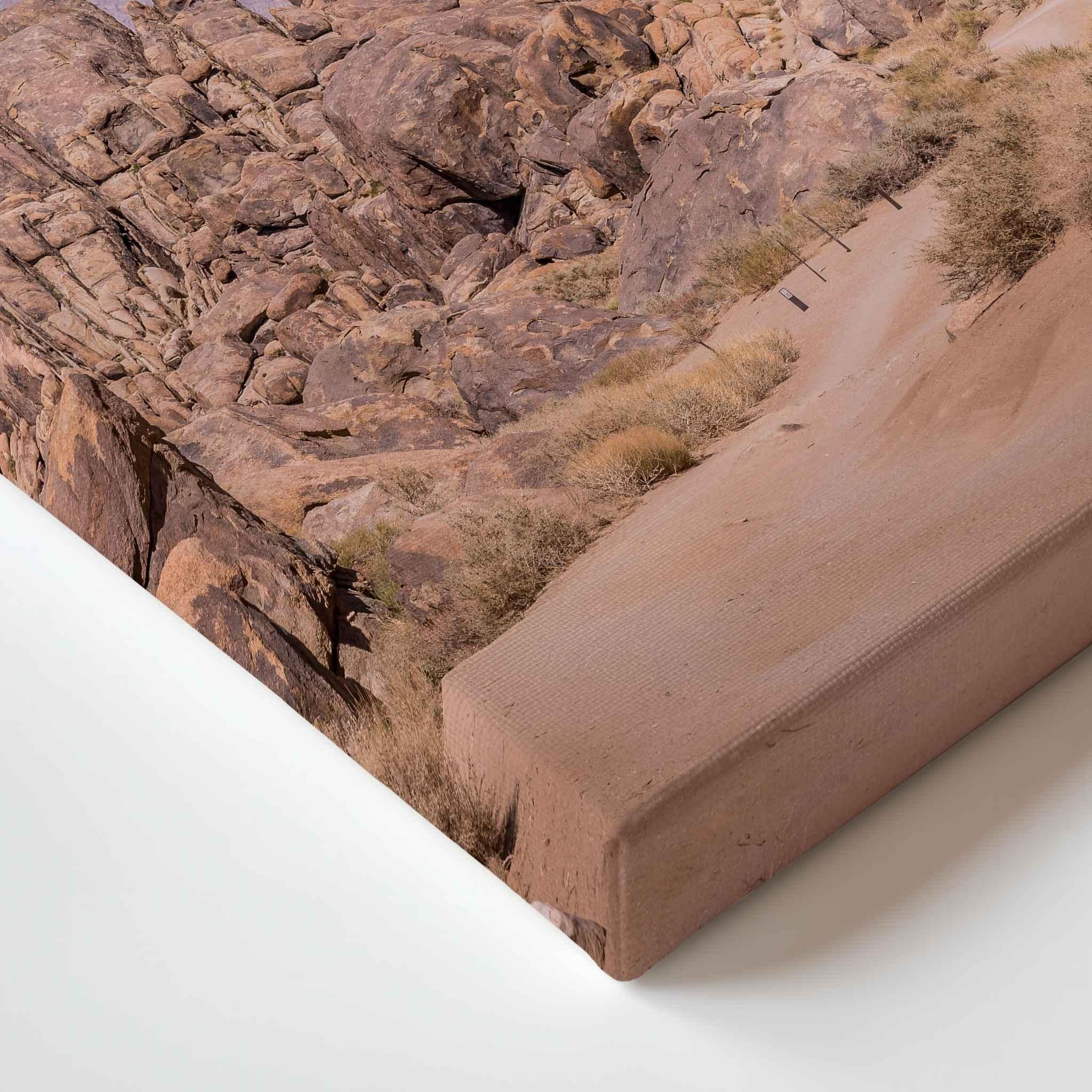 Close-up corner detail of Sierra Desert Path canvas print, showing the gallery-wrapped edge and warm desert landscape with a winding trail through rugged California rock formations.