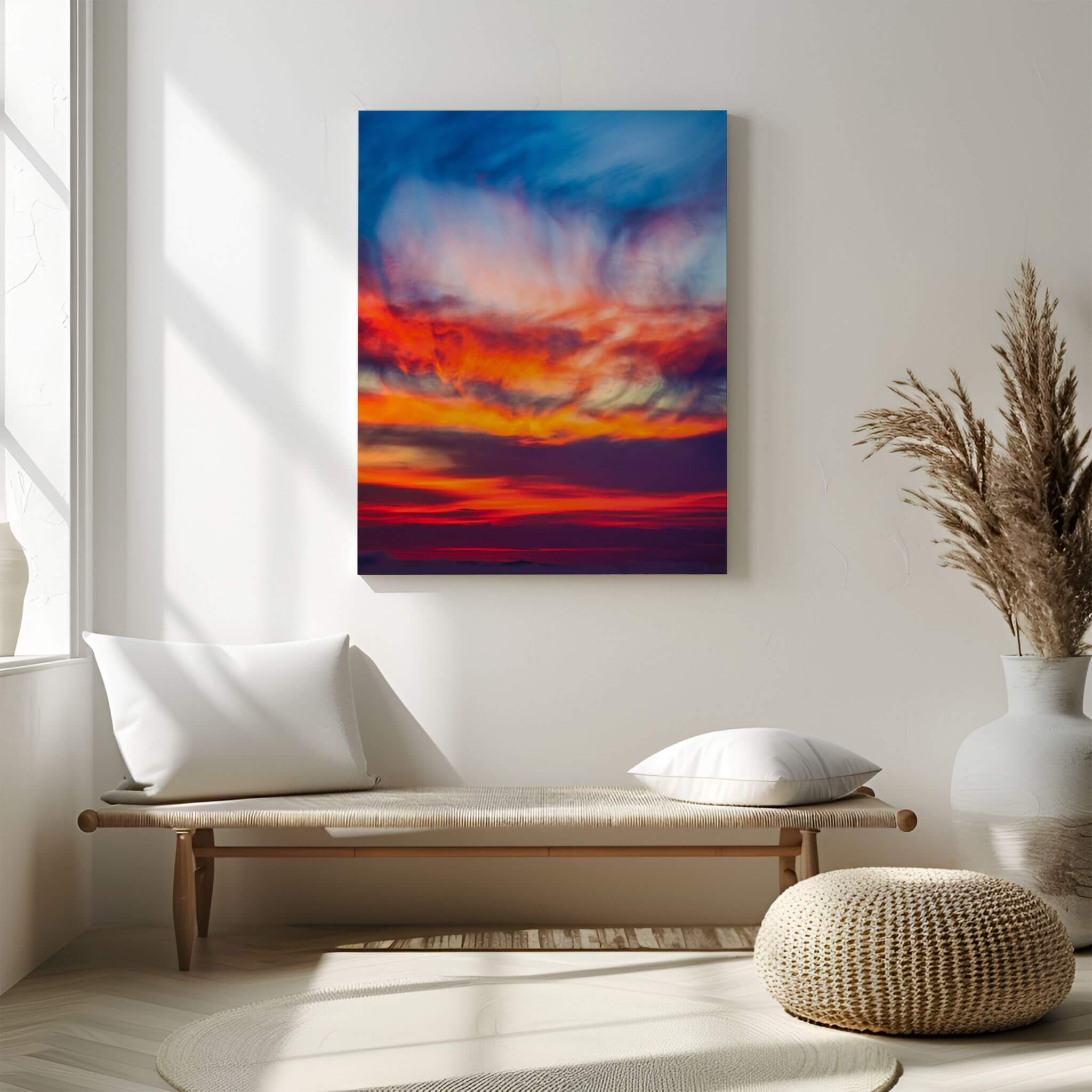 Smoldering Clouds high-definition metal print by Abigail Diane Photography displayed above a minimalist wood bench in a light neutral interior, showcasing dramatic cobalt blue, crimson, fiery orange, violet, and golden clouds at sunset over the Pacific Ocean in Southern California.