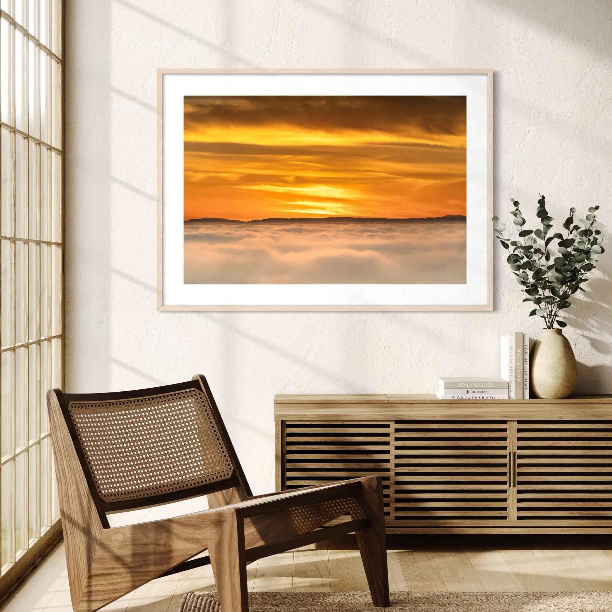 Soaring Above the Clouds framed fine art print displayed in a contemporary living room with natural wood furnishings, featuring a golden winter sunset above a sea of clouds. Artwork by Abigail Diane Photography.