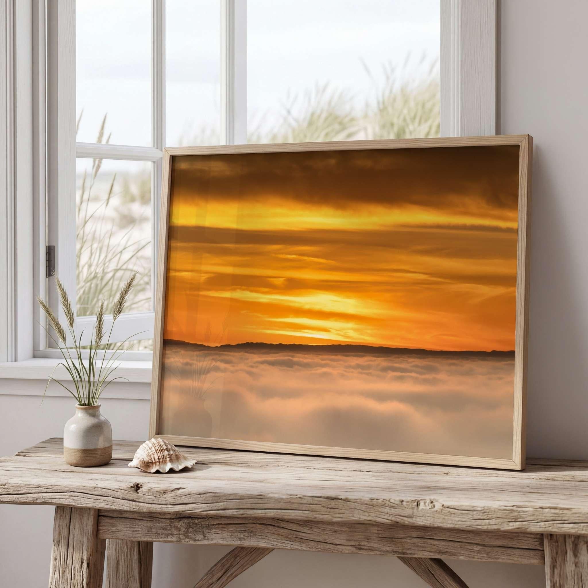 Soaring Above the Clouds framed fine art print displayed on a rustic wooden table beside a window, featuring a golden winter sunset above a sea of clouds. Artwork by Abigail Diane Photography.