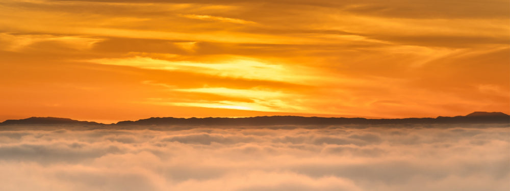 Soaring Above the Clouds by Abigail Diane Photography featuring a breathtaking golden sunset above a sea of clouds with distant mountain silhouettes viewed from Laguna Beach, California.