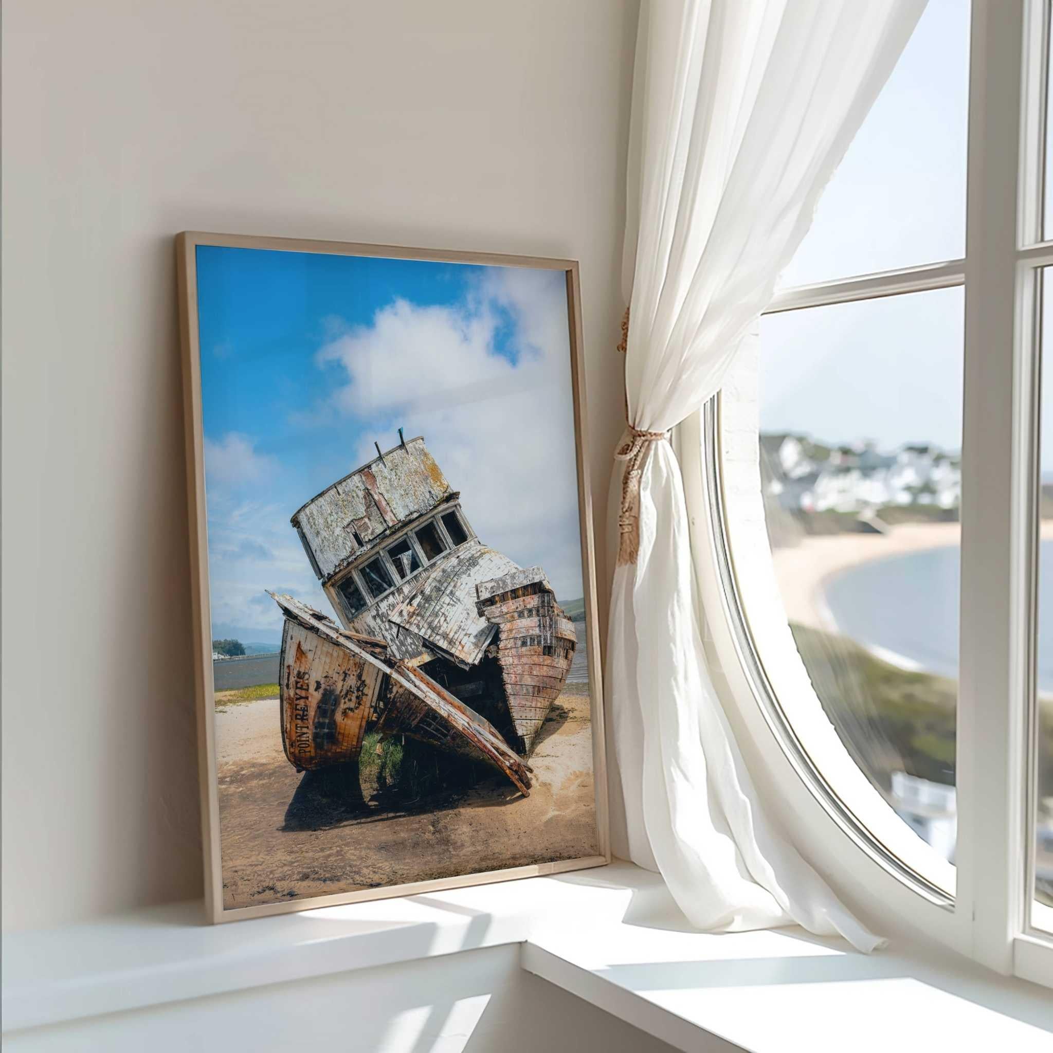 Framed S.S. Point Reyes shipwreck fine art photograph displayed beside a round coastal window with flowing white curtains, with a view of the water by Abigail Diane Photography.