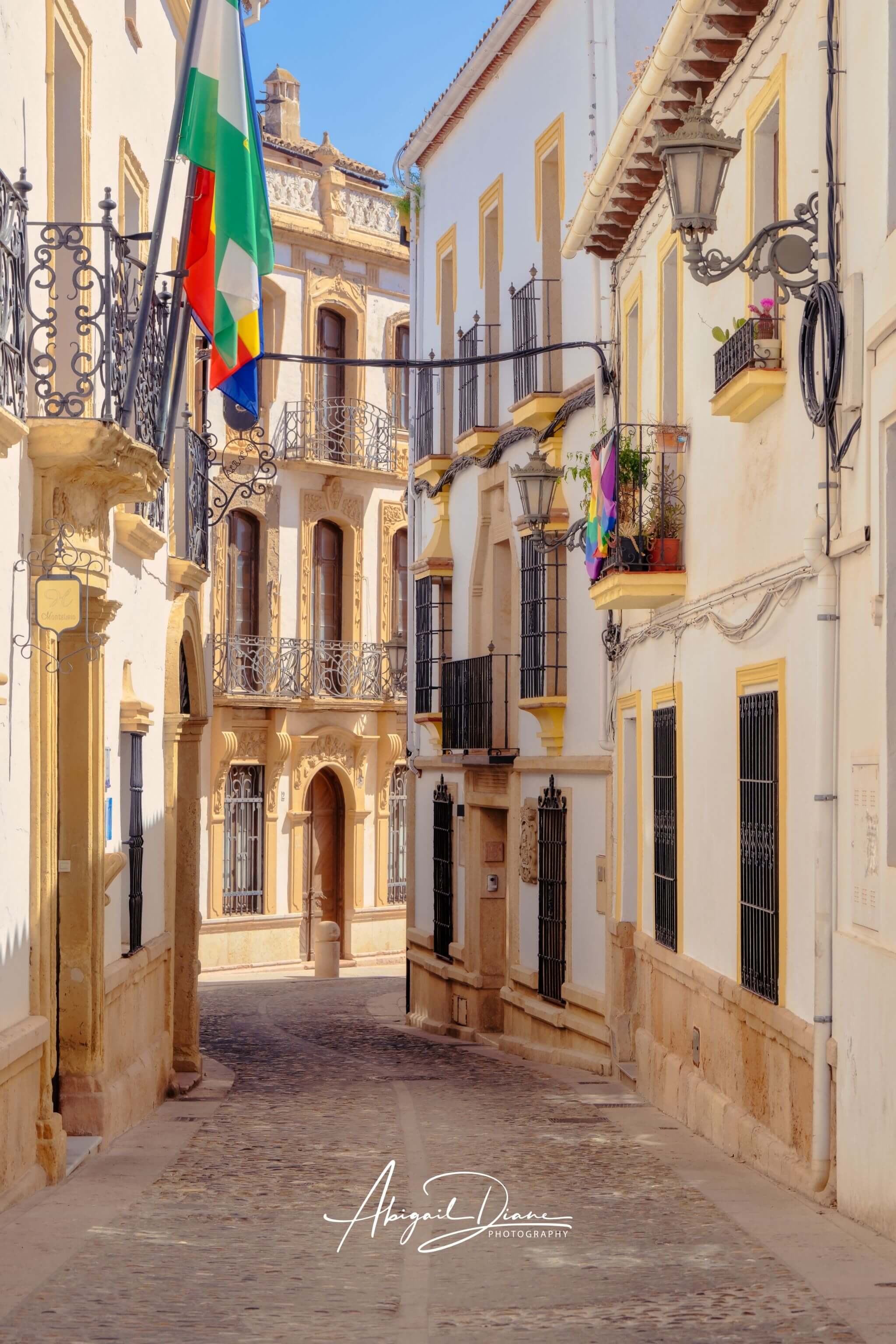 Streets of Ronda featuring a sunlit cobblestone street, whitewashed buildings and ornate Andalusian architecture in Ronda, Spain – Abigail Diane Photography