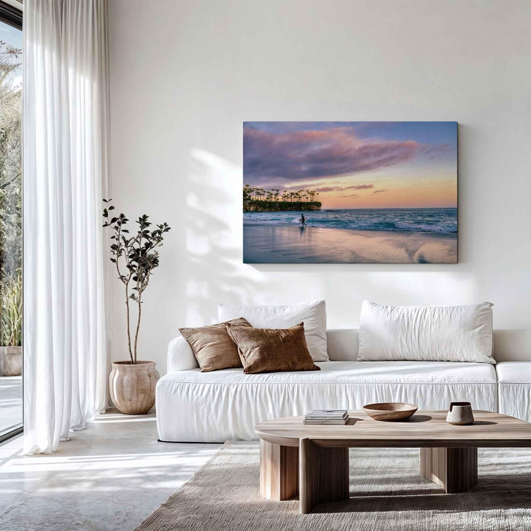 Large Surfing a California Sunset canvas wall art by Abigail Diane Photography displayed in a modern living room above a sofa, featuring a surfer, pastel sunset skies, and Crescent Beach in Laguna Beach, California.
