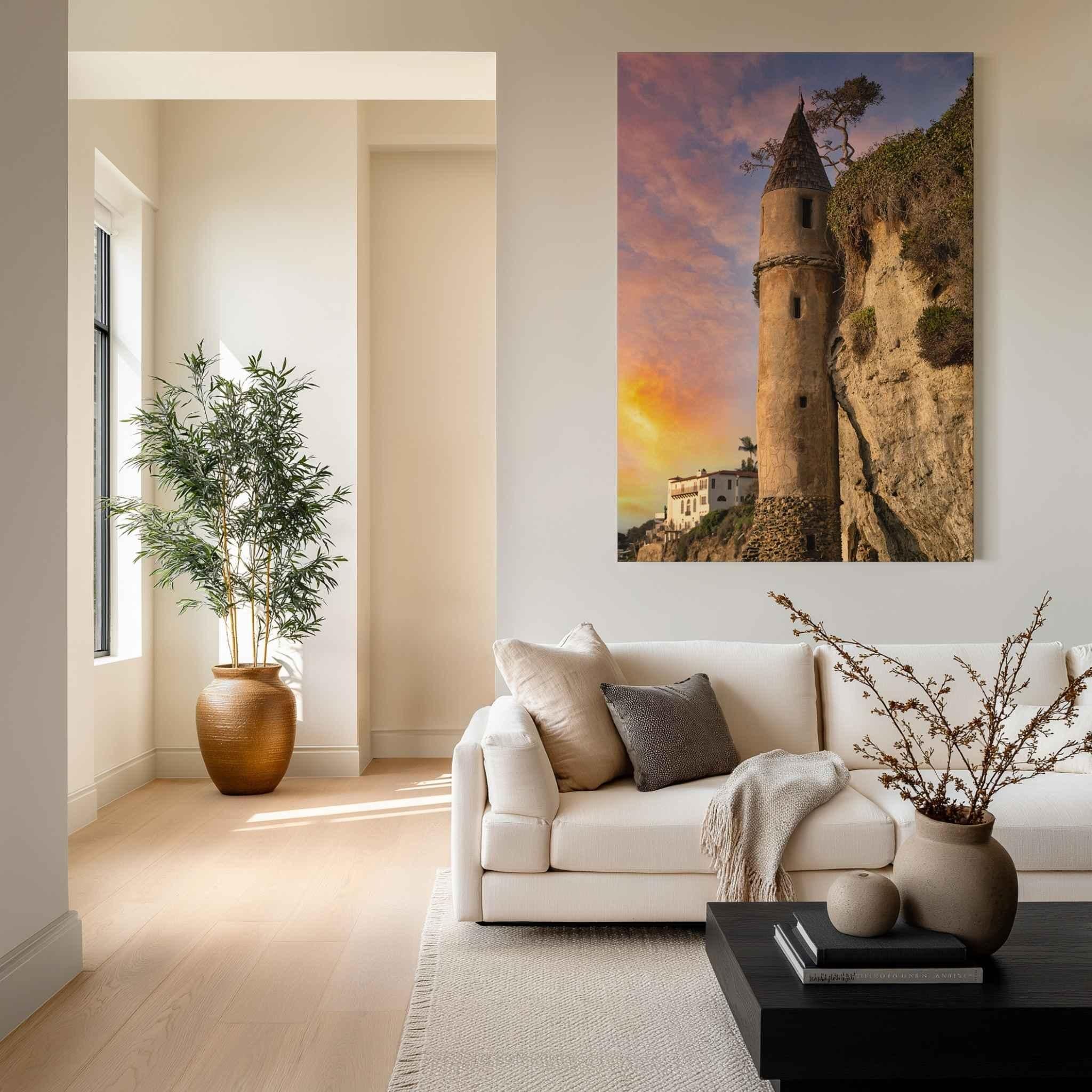 Chromaluxe High Definition Metal print of Victoria Beach Pirate Tower at sunset in Laguna Beach, California, displayed above a contemporary cream sofa in a warm modern living room with soft natural light and minimalist décor.