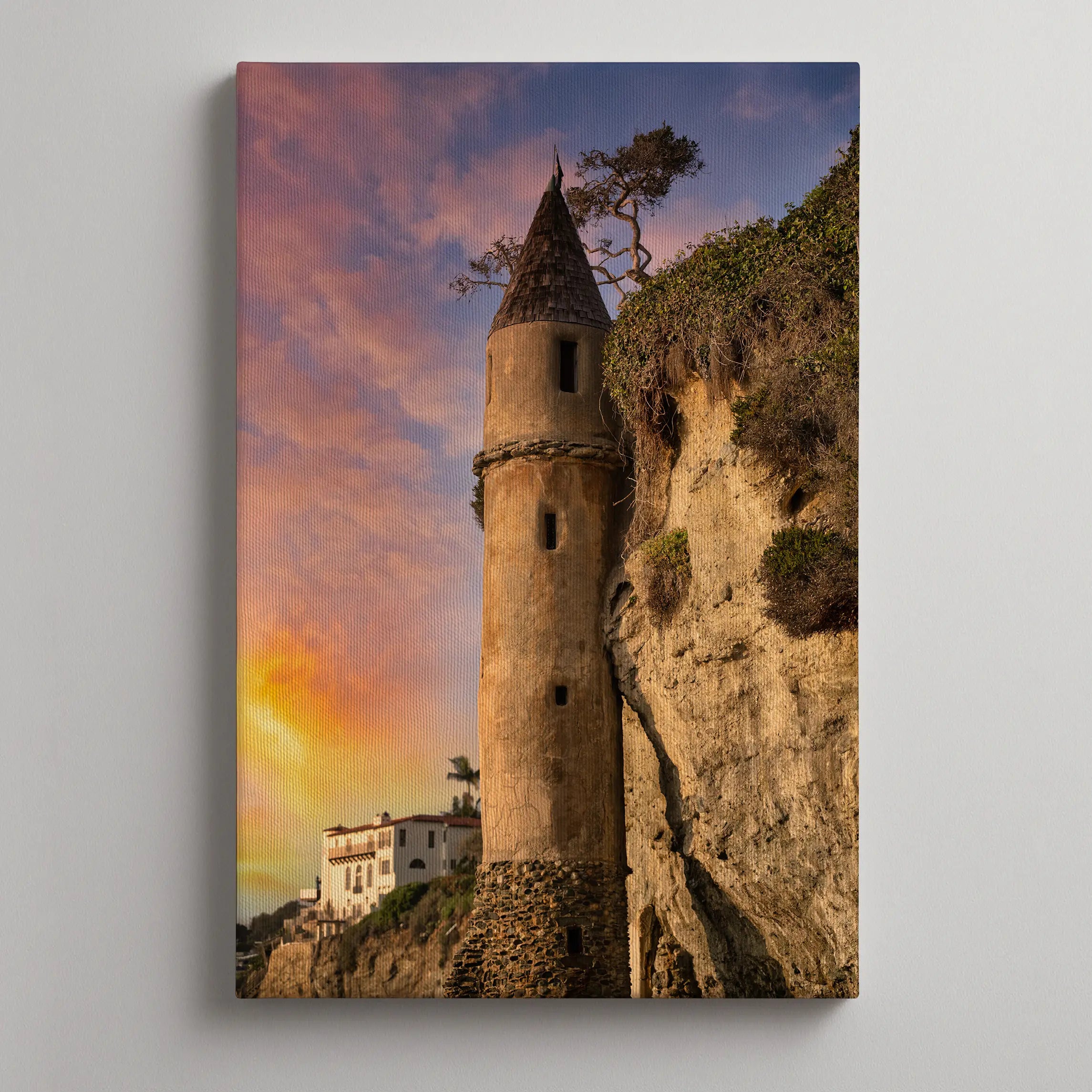 Gallery wrapped canvas print of Victoria Beach Pirate Tower at sunset in Laguna Beach, California, displayed on a soft warm gallery wall. Golden evening light, pastel sky, and rugged coastal cliffs create an elegant coastal wall art mockup.