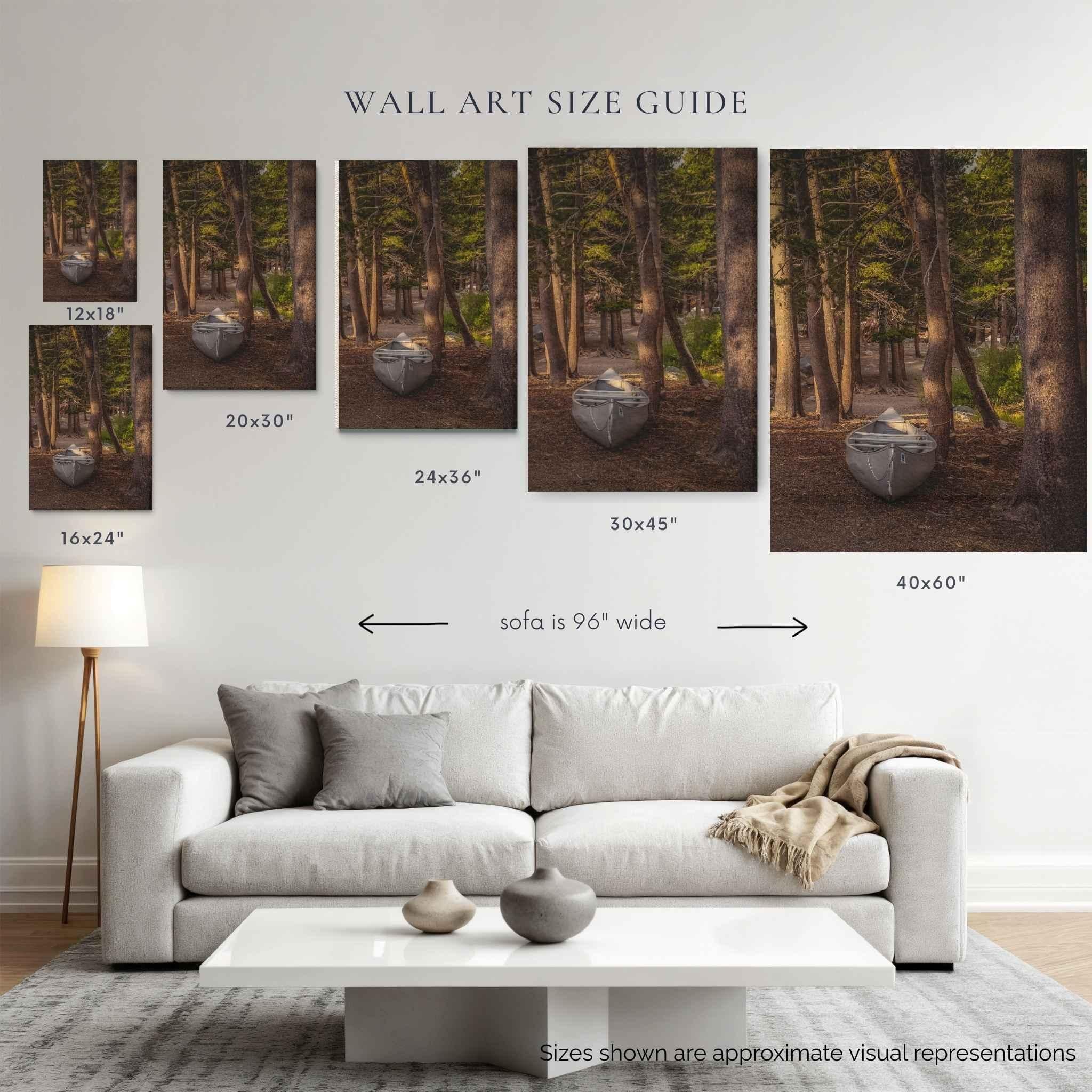 A wall art size guide showing six canvas prints of a forest cabin scene, labeled with dimensions from 12x18 to 40x60 inches, above a modern white sofa in a styled living room.