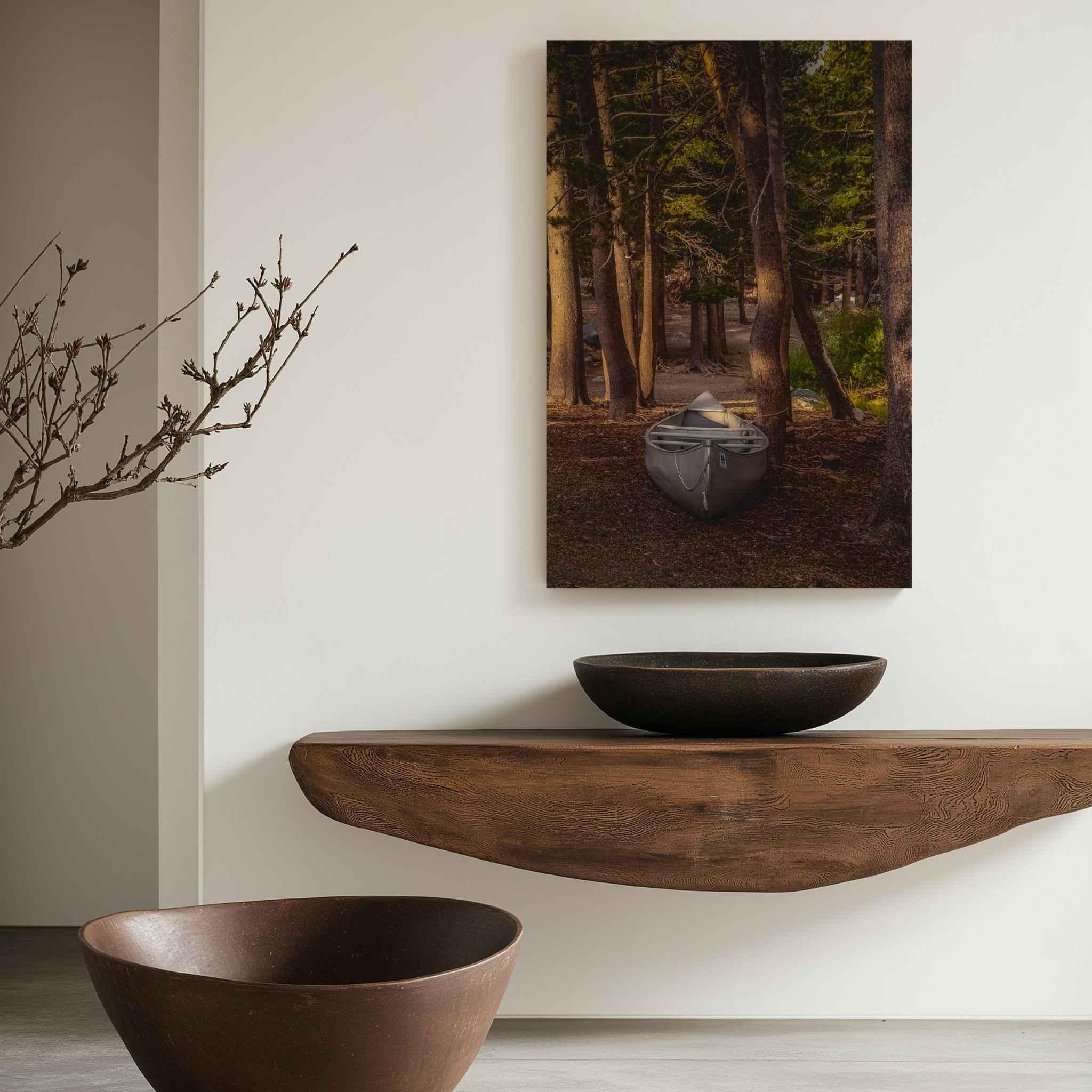 Waiting for the Water metal print displayed above a natural wood console in a minimalist interior, featuring a canoe among pine trees near Mammoth Lakes, California.