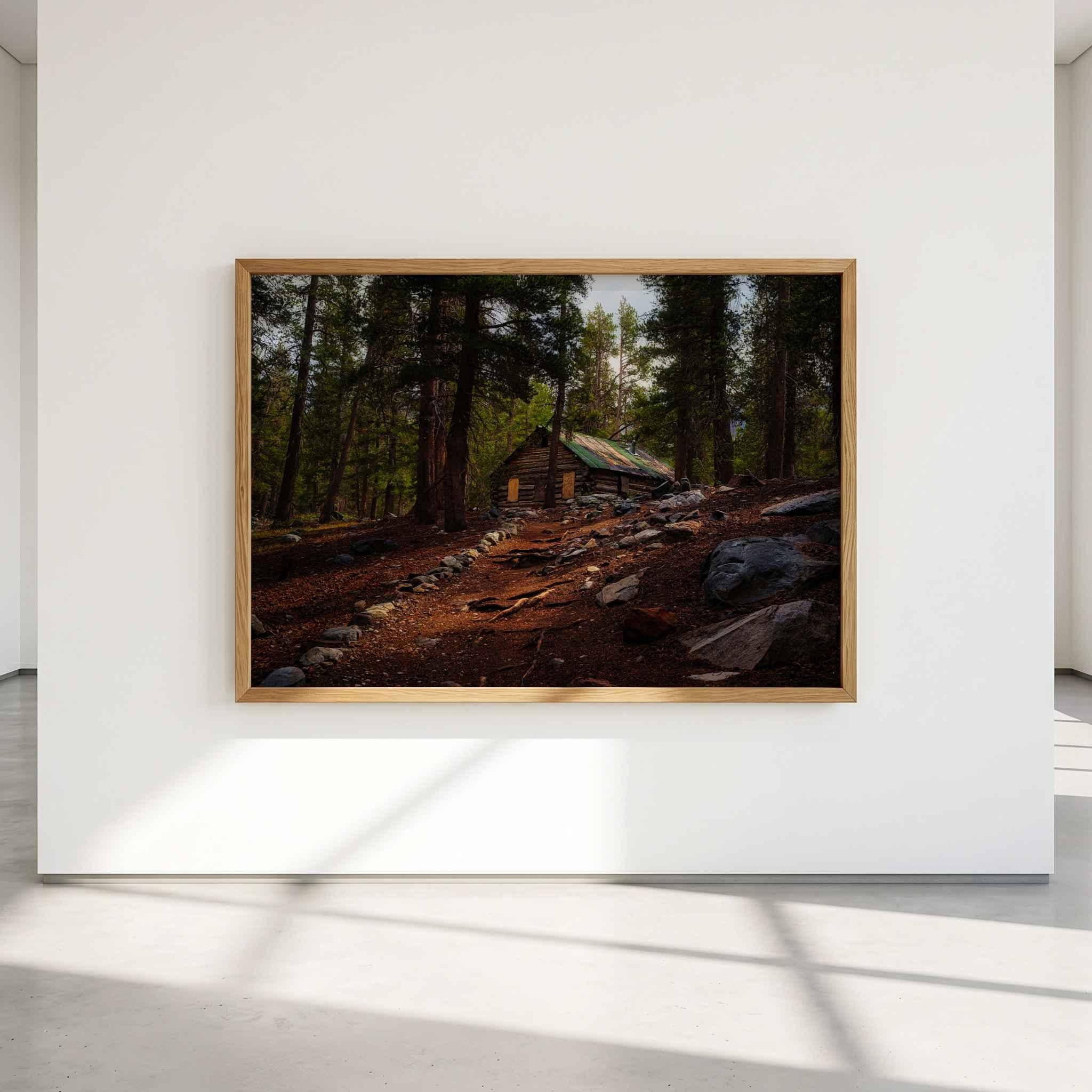 Where the Trail Meets the Past fine art print featuring historic Mahan Cabin surrounded by forest near Mammoth Lakes in California’s Eastern Sierra, displayed in a natural wood frame on a minimalist gallery wall.