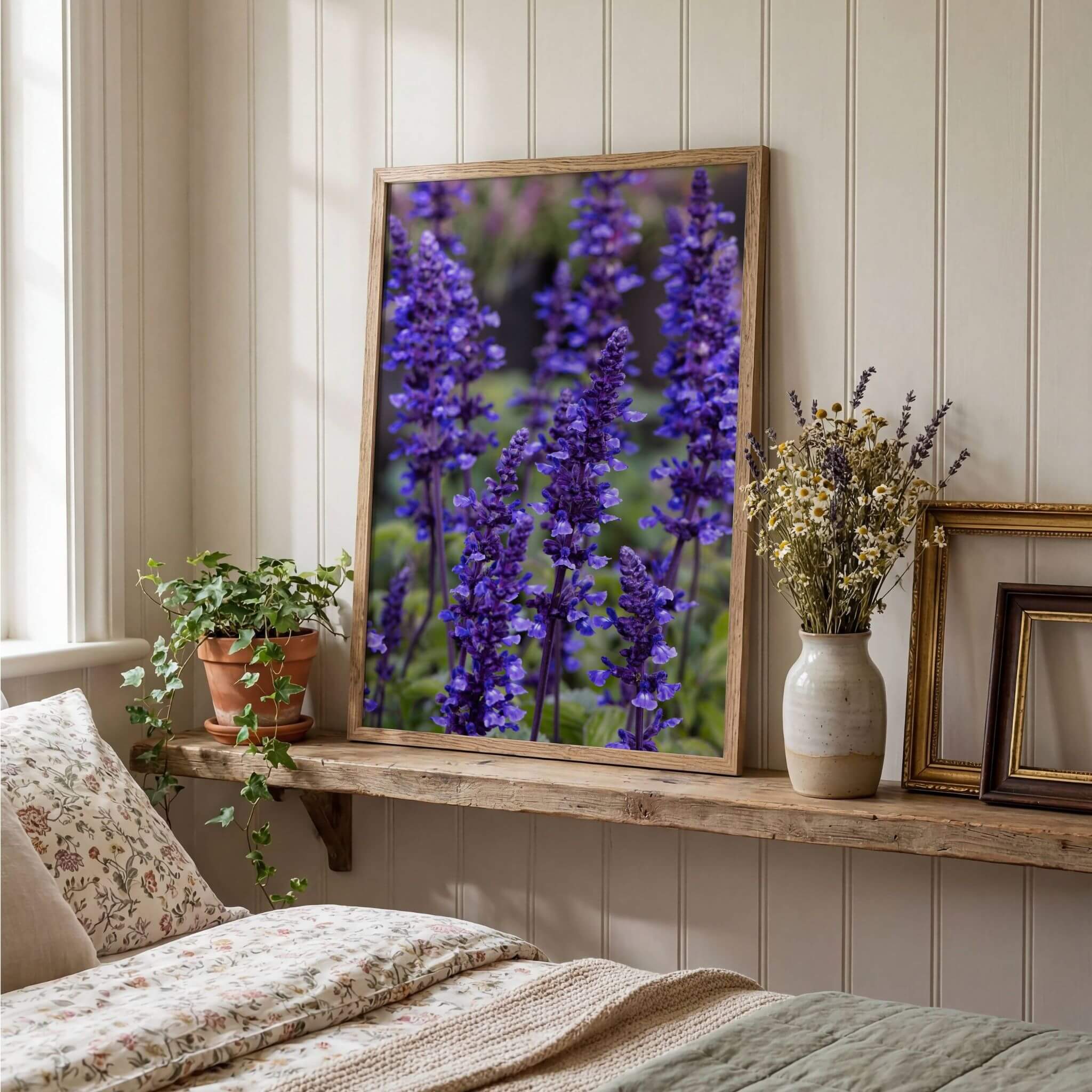 Where the Wildflowers Dream by Abigail Diane Photography displayed in a natural oak frame on a rustic wooden shelf above a cottage-style bed, featuring vibrant purple salvia flowers and soft botanical décor.