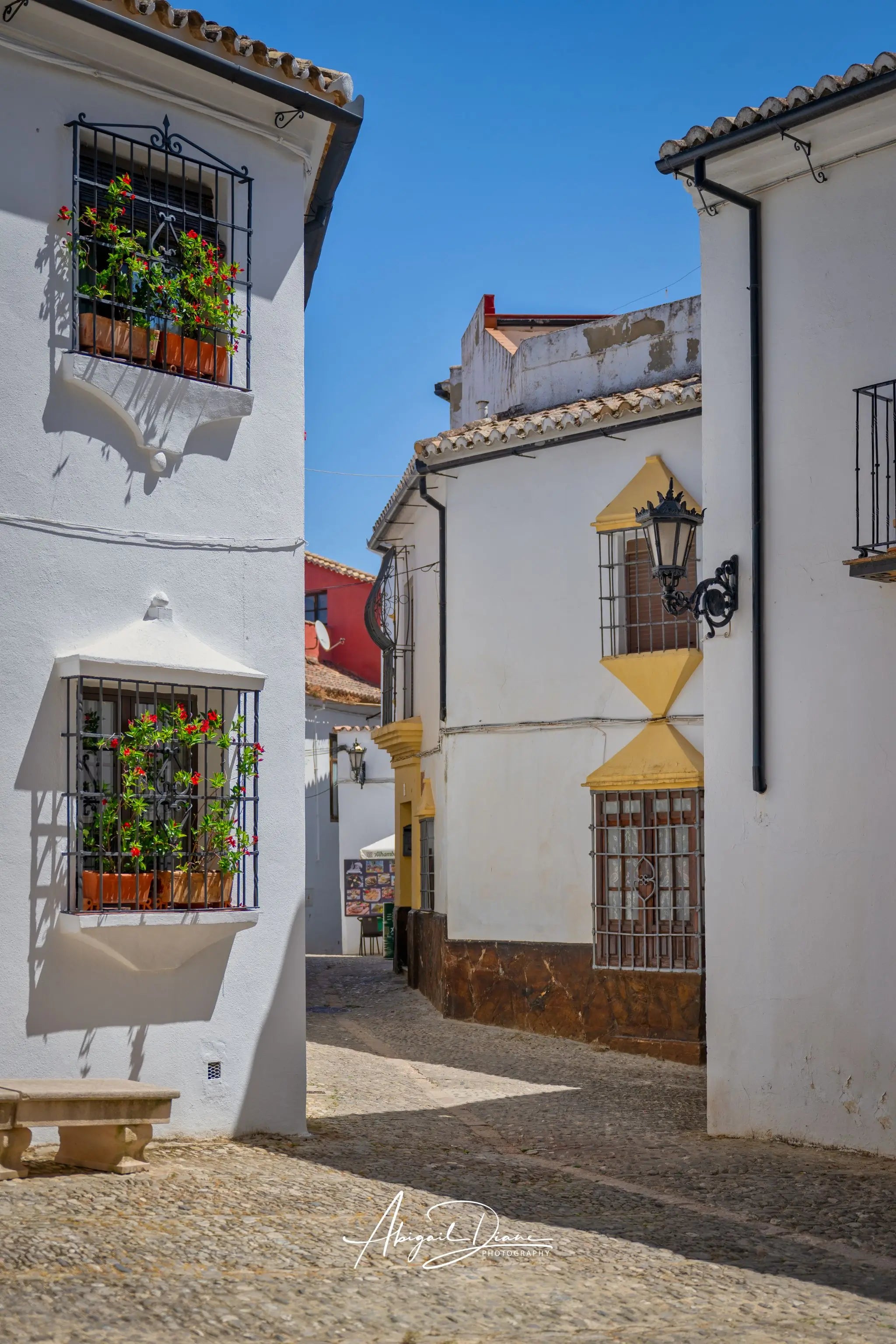 Whitewashed Streets of Setenil showing a cobbled street, flower-filled windows, and traditional white houses in Setenil de las Bodegas, Andalucía, Spain.  Photography Photographed by Abigail Diane Photography.
