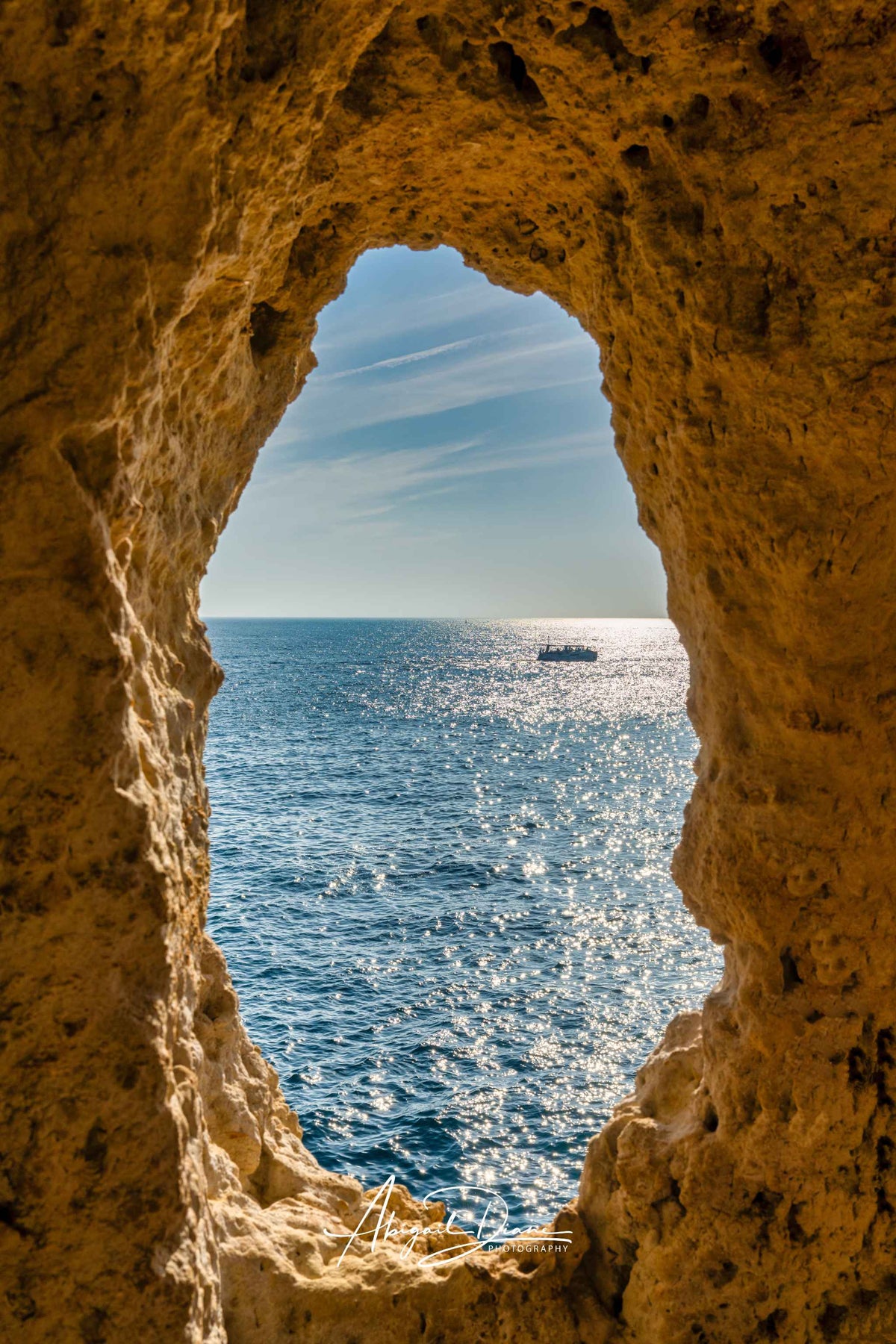 Window to the Atlantic at Algar Seco in the Algarve, Portugal, framed by golden limestone cliffs overlooking the blue Atlantic Ocean. Photographed by Abigail Diane Photography.