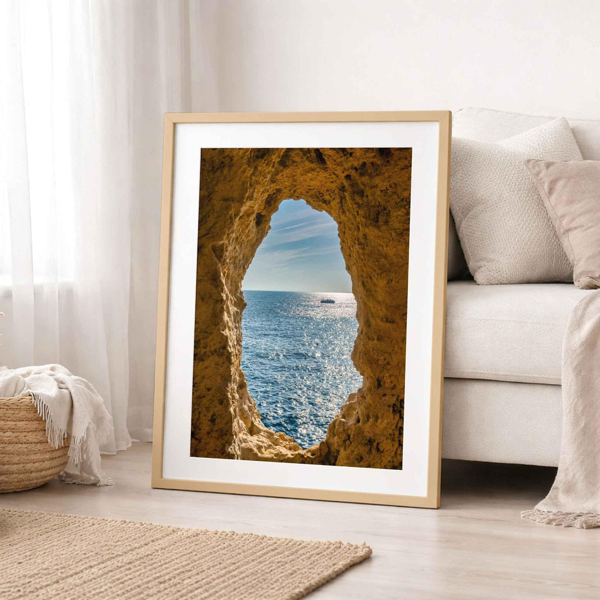  Framed Window to the Atlantic print of Algar Seco, Algarve, Portugal, styled beside a sofa in a soft neutral coastal interior.